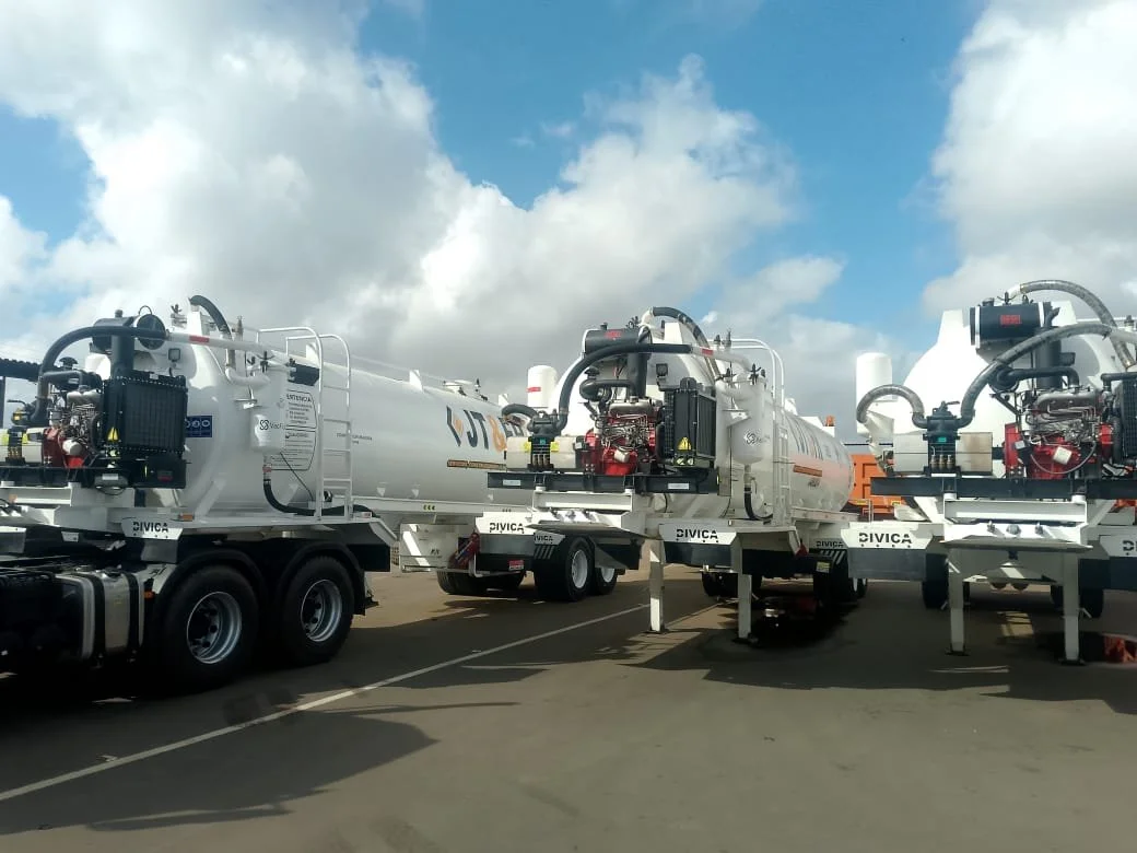 Tres camiones cisterna blancos en una fila en un área pavimentada, con cielo parcialmente nublado en el fondo.