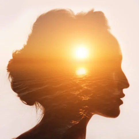 Overlayed images, one of a women's face and the other image of a sun setting over the sea