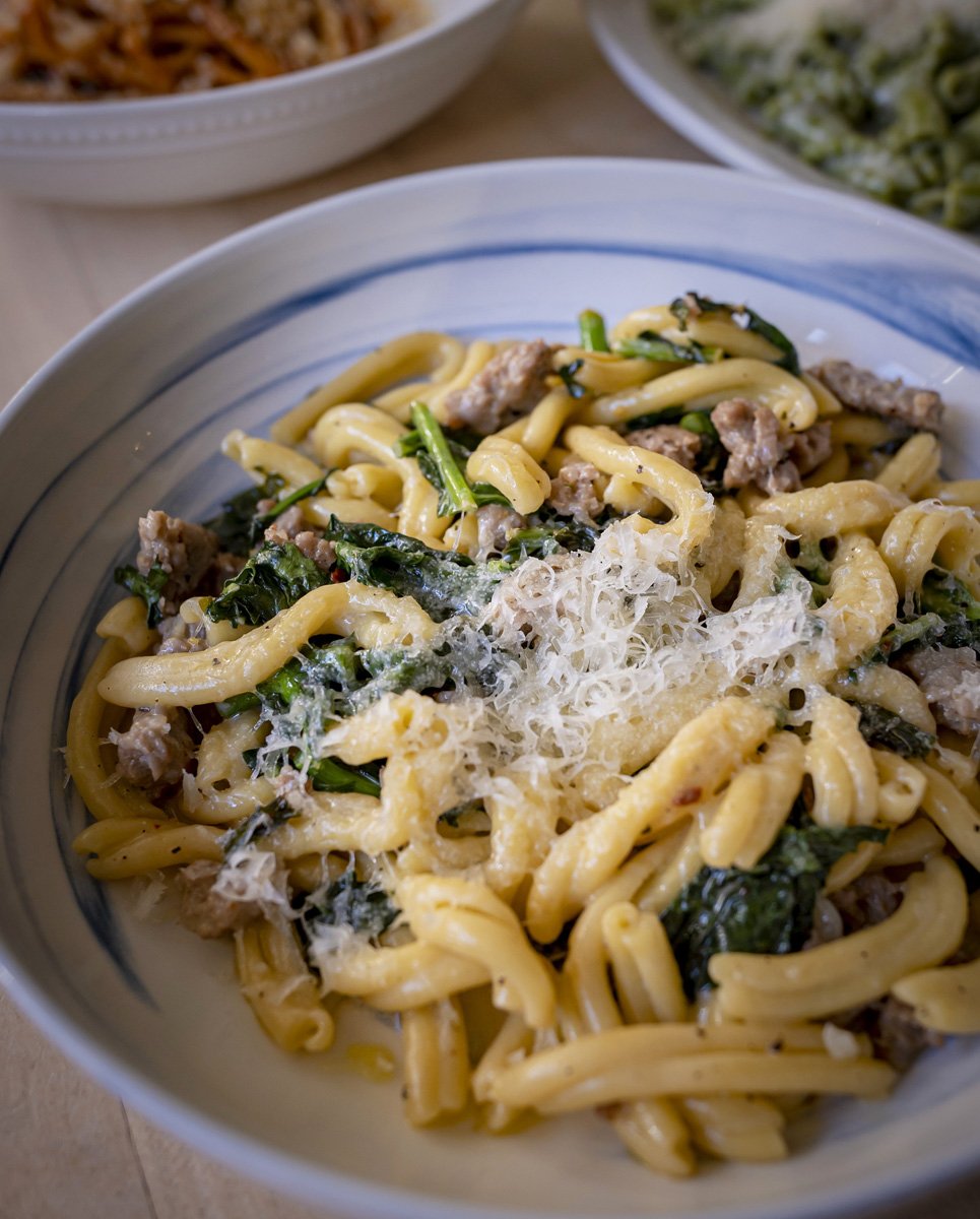 A bowl of pasta with sausage, vegetables, and grated cheese.