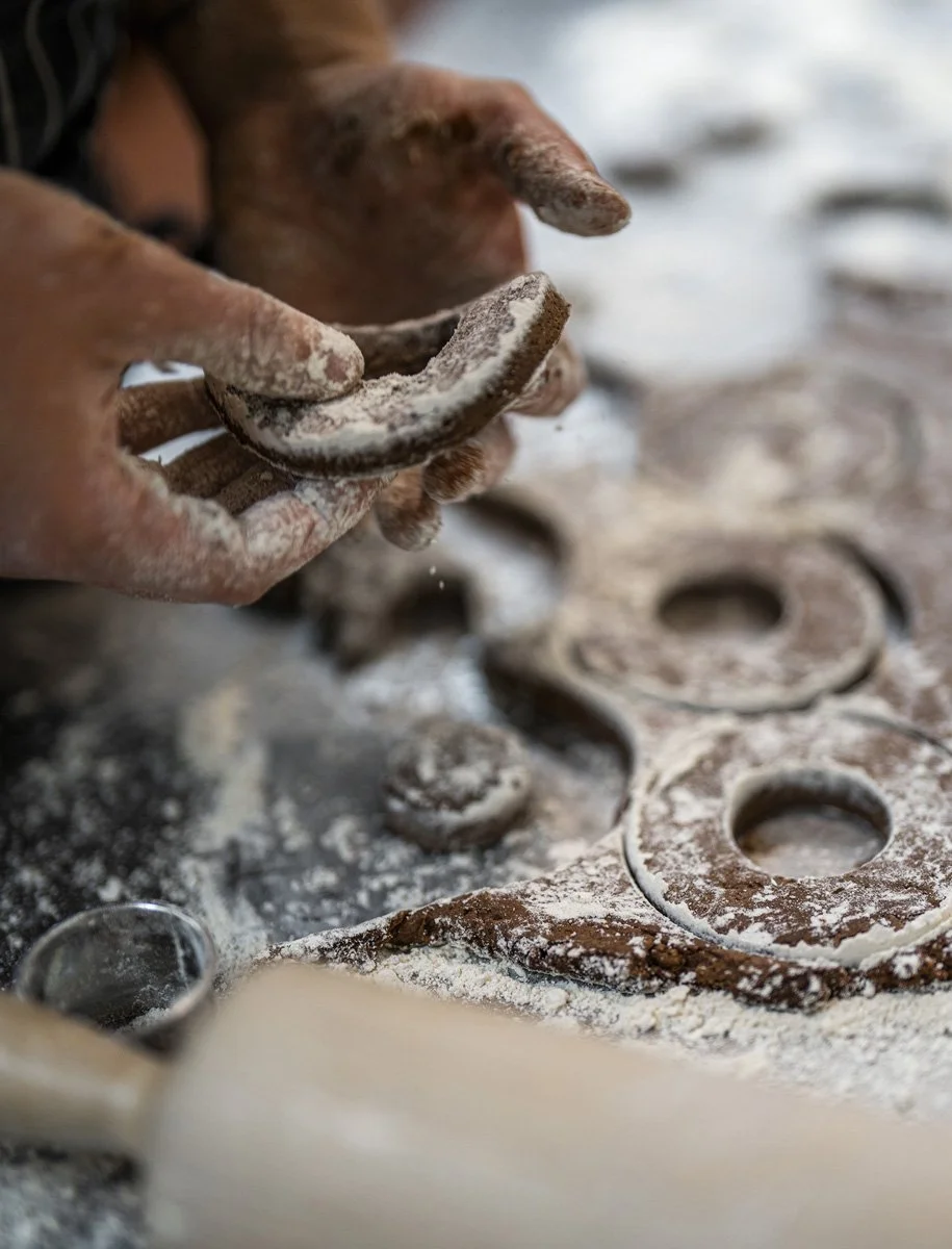 Close-up of hands shaping doughnut dough with ring cutters on a floured surface.