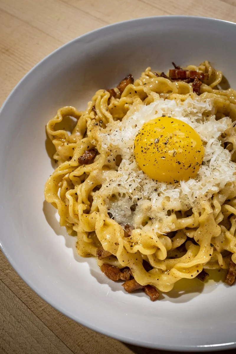 A bowl of cooked pasta topped with a raw egg yolk and grated cheese.