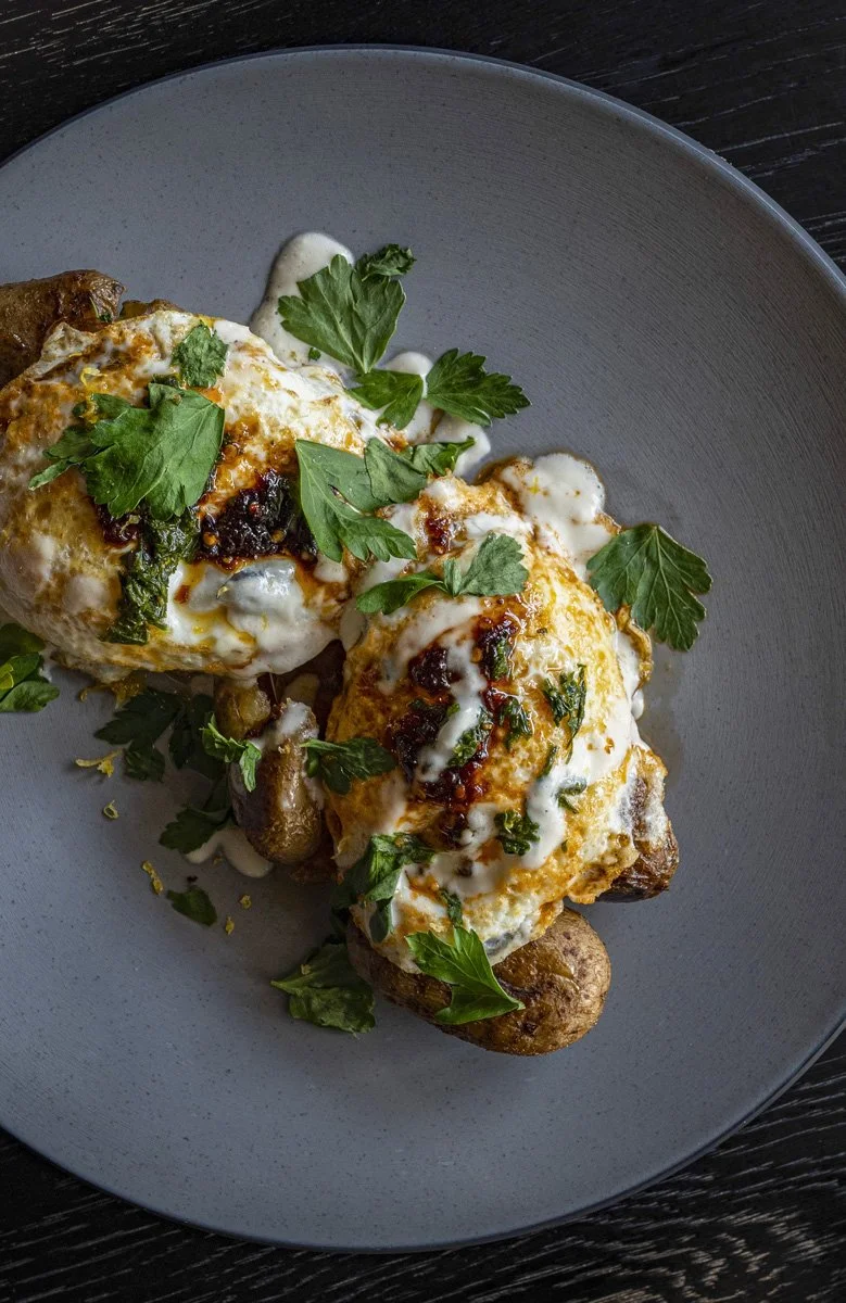 Over easy eggs topped with some cream sauce, garnished with fresh green parsley, on a gray plate.