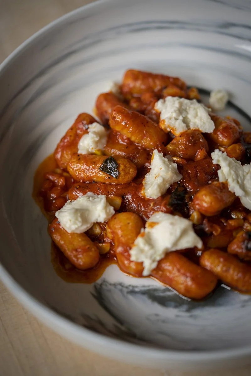Close-up of a bowl of gnocchi with spicy N'duja sauce and dollops of whipped ricotta. 