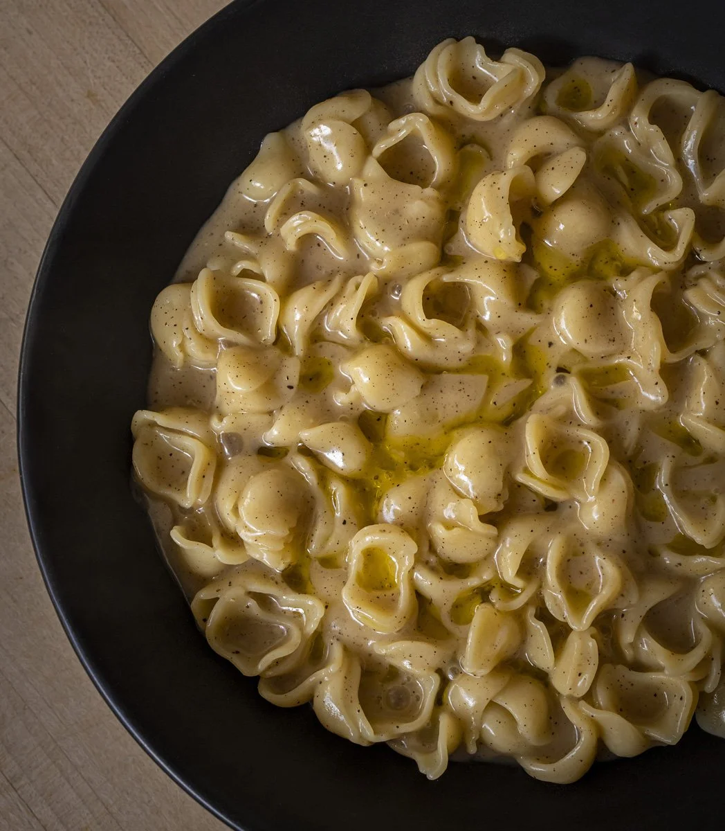 Creamy cheese with shells pasta with black pepper in a black bowl