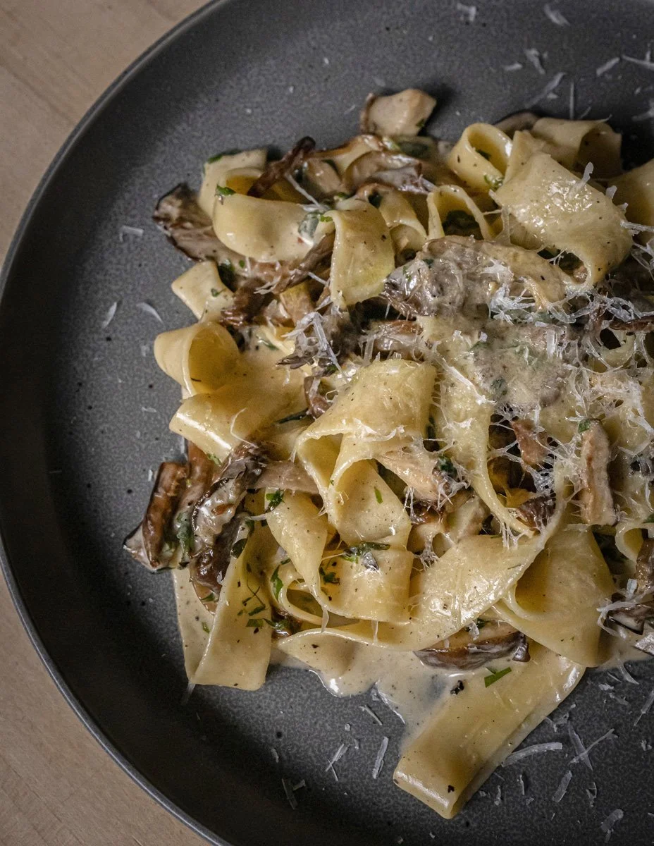 Pasta with cream sauce, mushrooms, shredded cheese, and herbs on a dark plate.