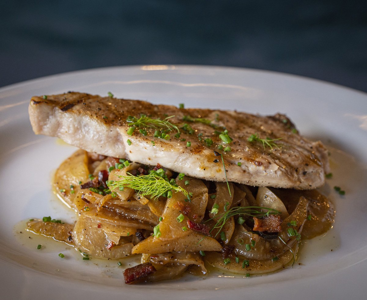 A plate of cooked fish fillet garnished with fresh herbs, served over sautéed vegetables on a white plate.