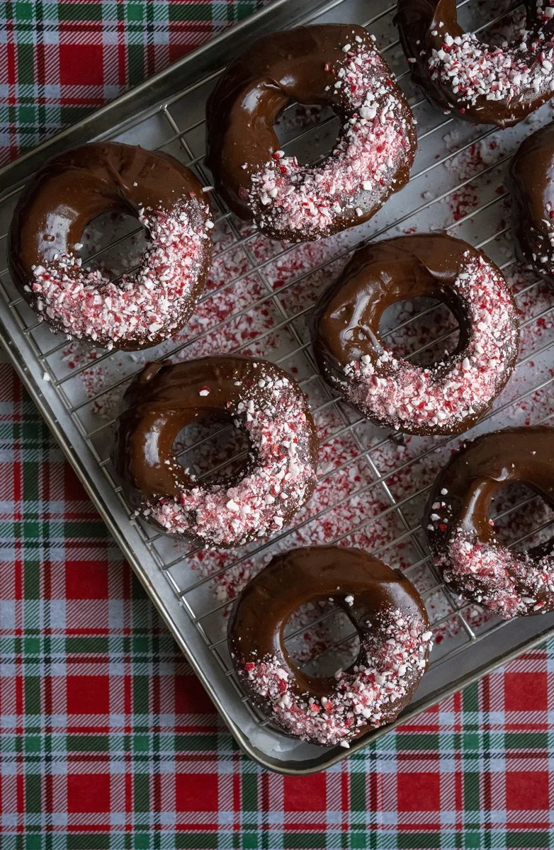 Chocolate-glazed donuts topped with crushed peppermint candies on a metal cooling rack.