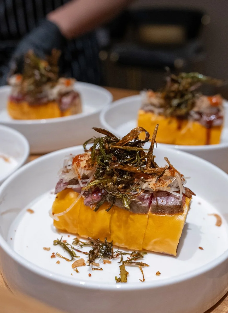 A fancy sushi roll with seared beef filet slices on top.