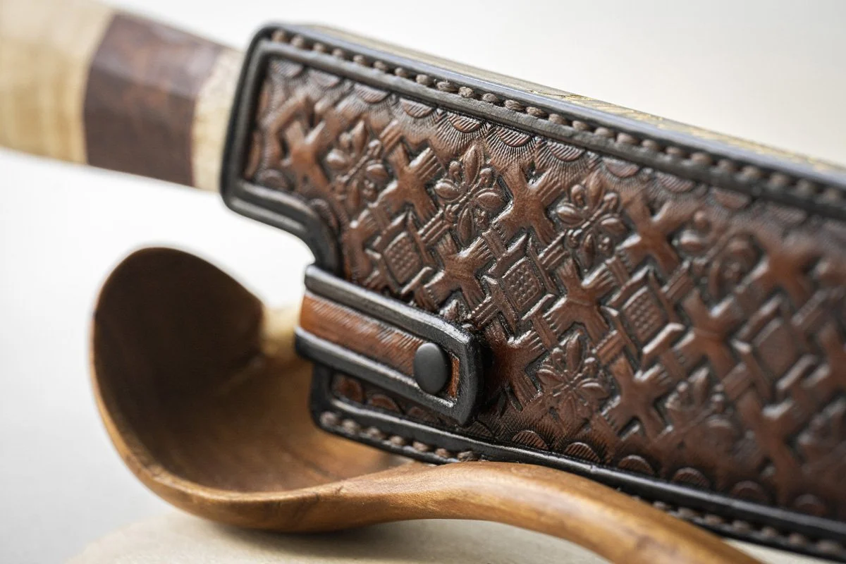Close-up of a leather wallet with intricate carved patterns, resting on a wooden spoon.