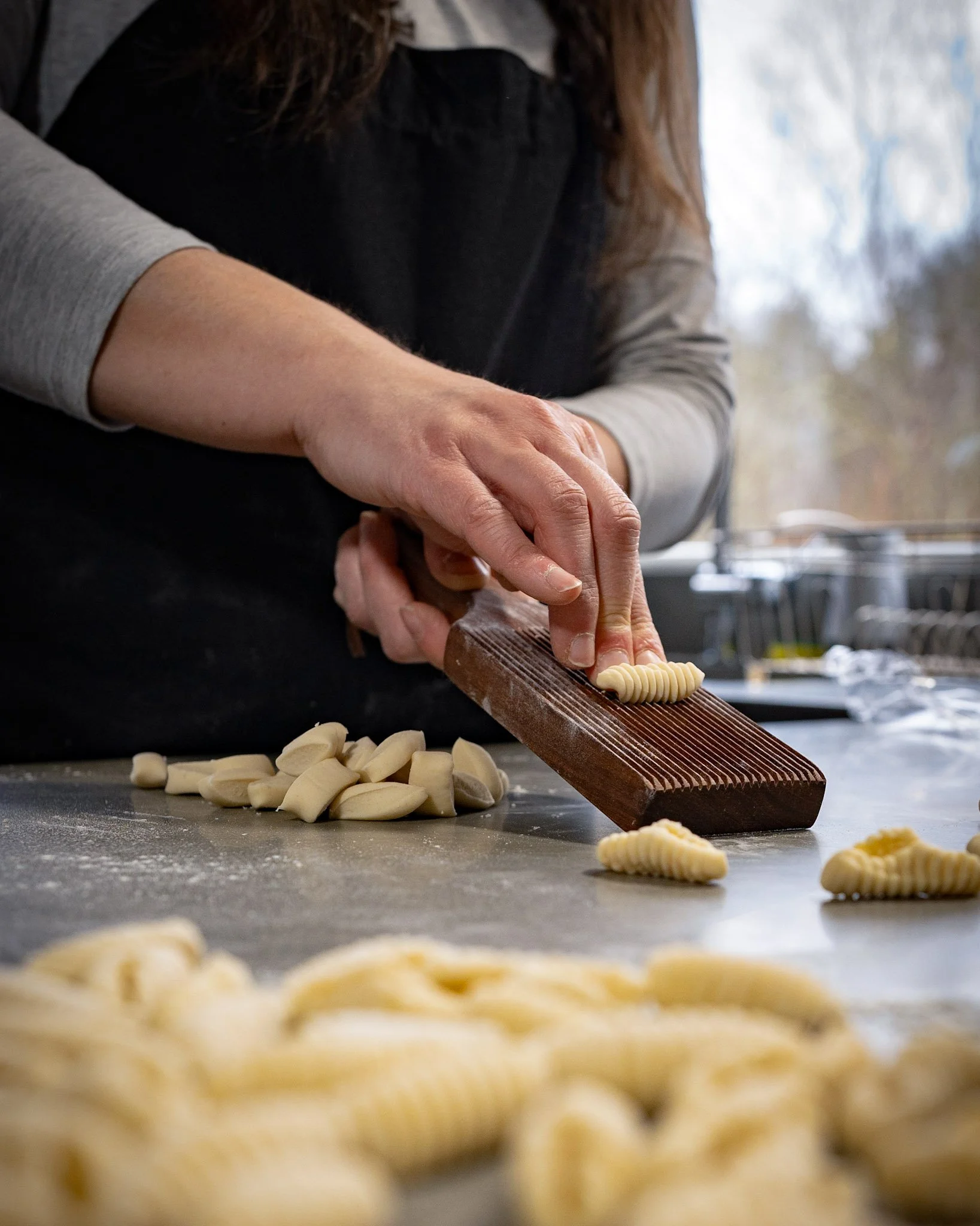 Young woman rolling fresh cavatelli pasta on a wooden gnocchi board.