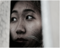 Close-up of a person's face peering through a window or curtain.
