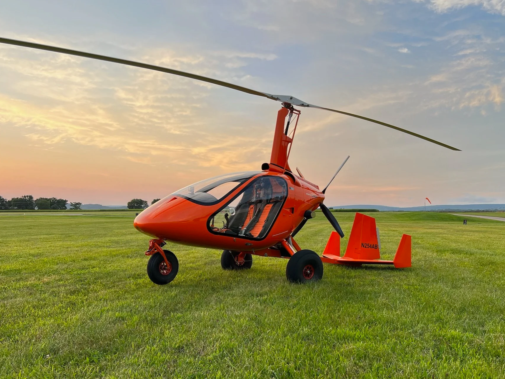 Orange M24 parked on a grassy airfield at sunset with open fields and a windsock in the background.