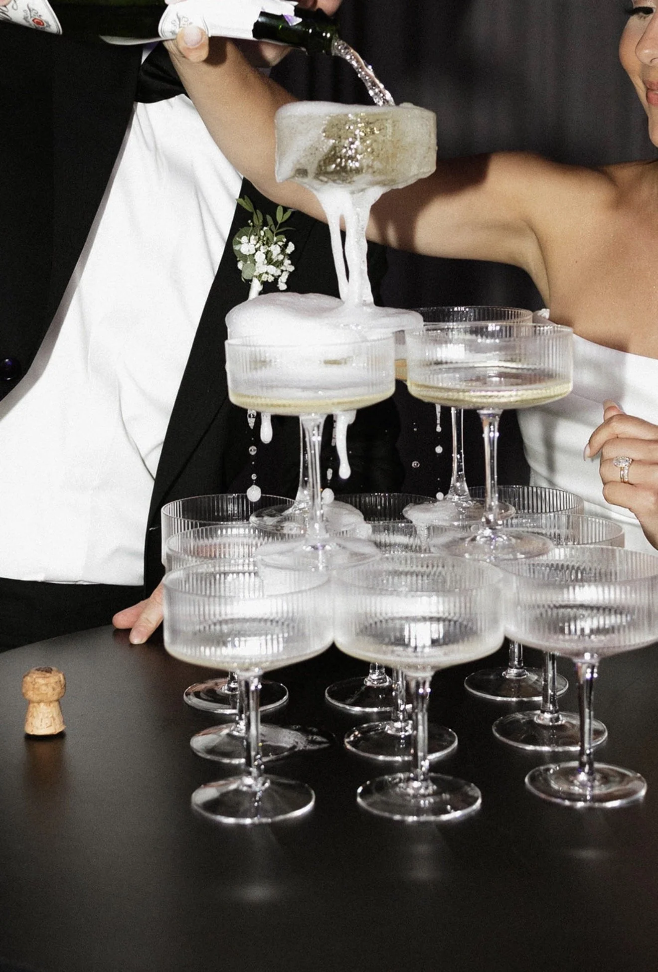 Champagne being poured into coupe glasses, creating a dramatic foamy overflow at a wedding celebration
