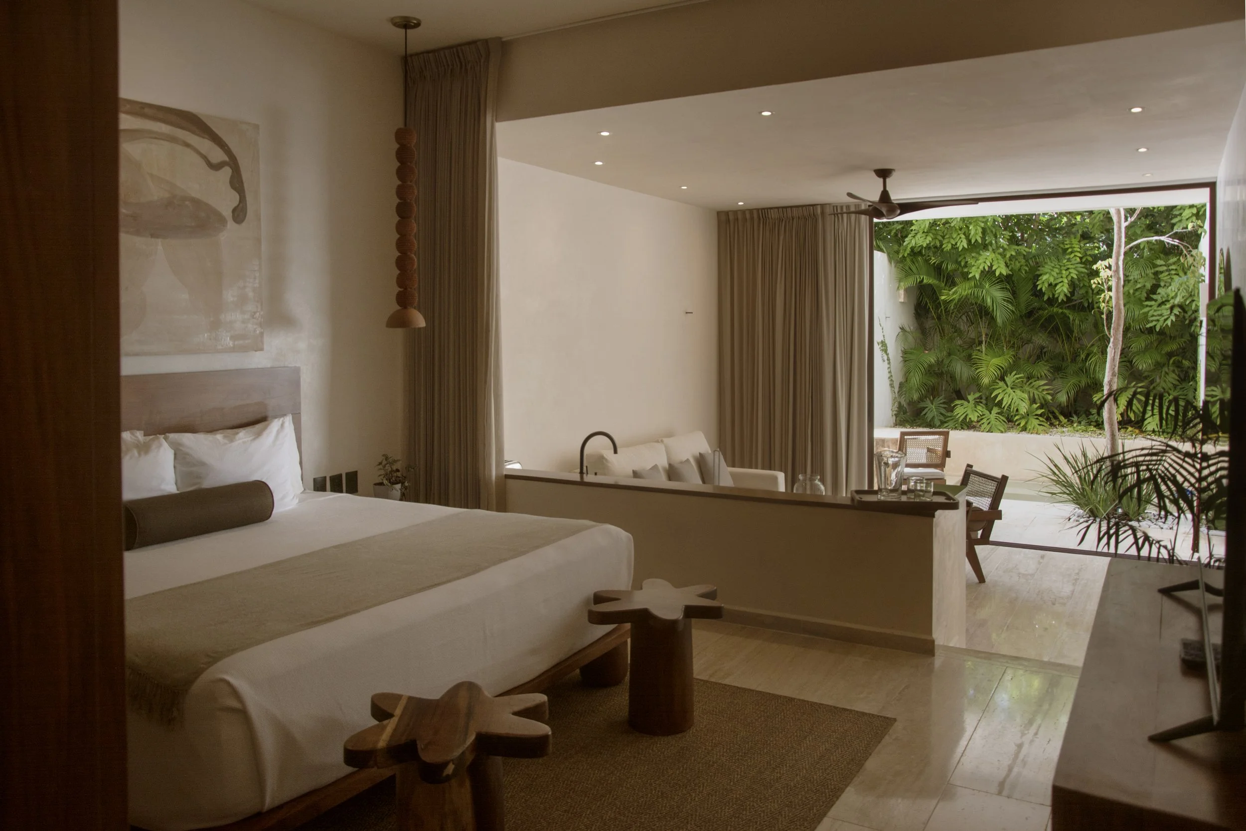Hotel room with garden and pool, with artistic design in beige tones featuring sofa, bed, chairs, and decorative elements