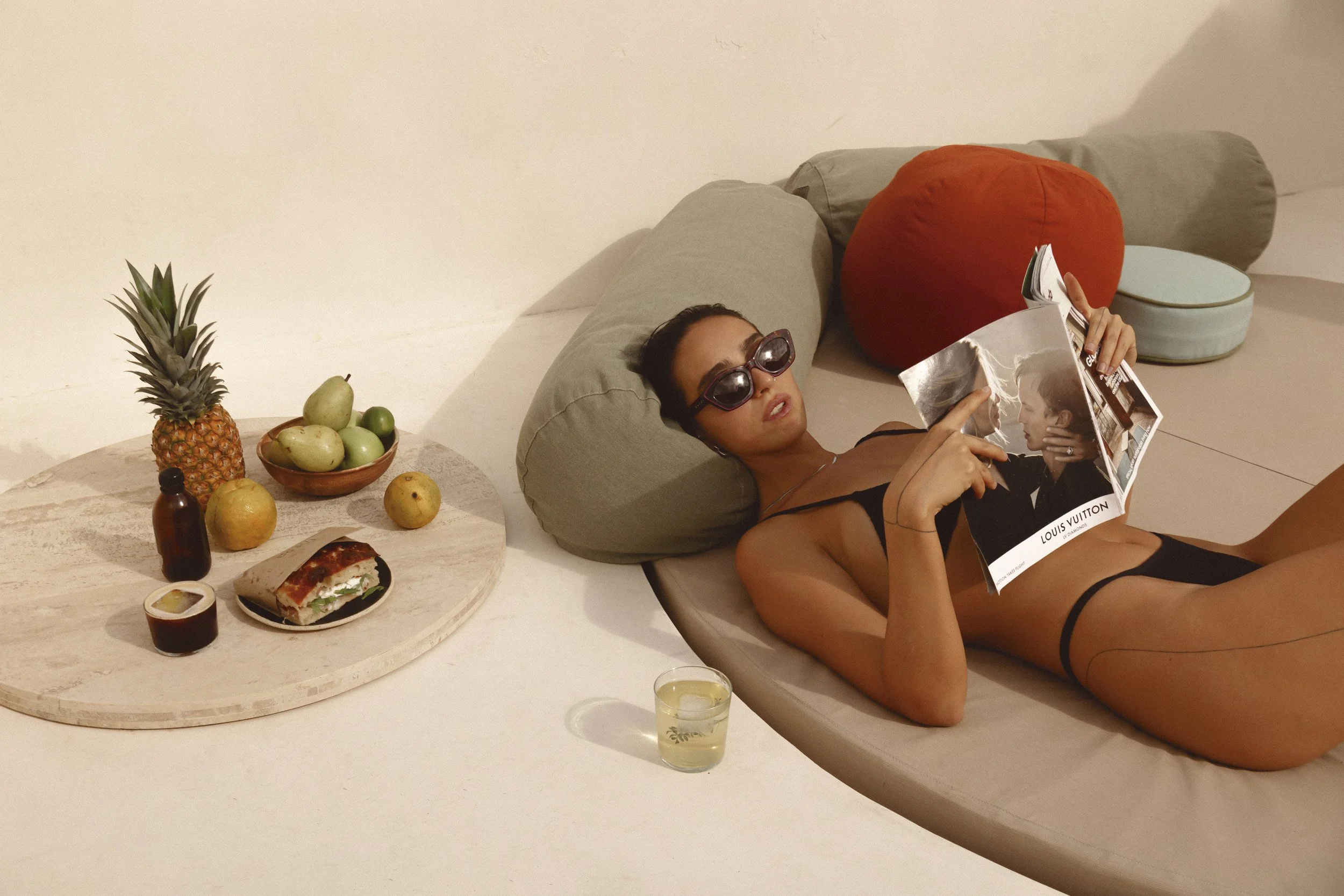 Woman sunbathing by the pool wearing sunglasses with fruit and coffee