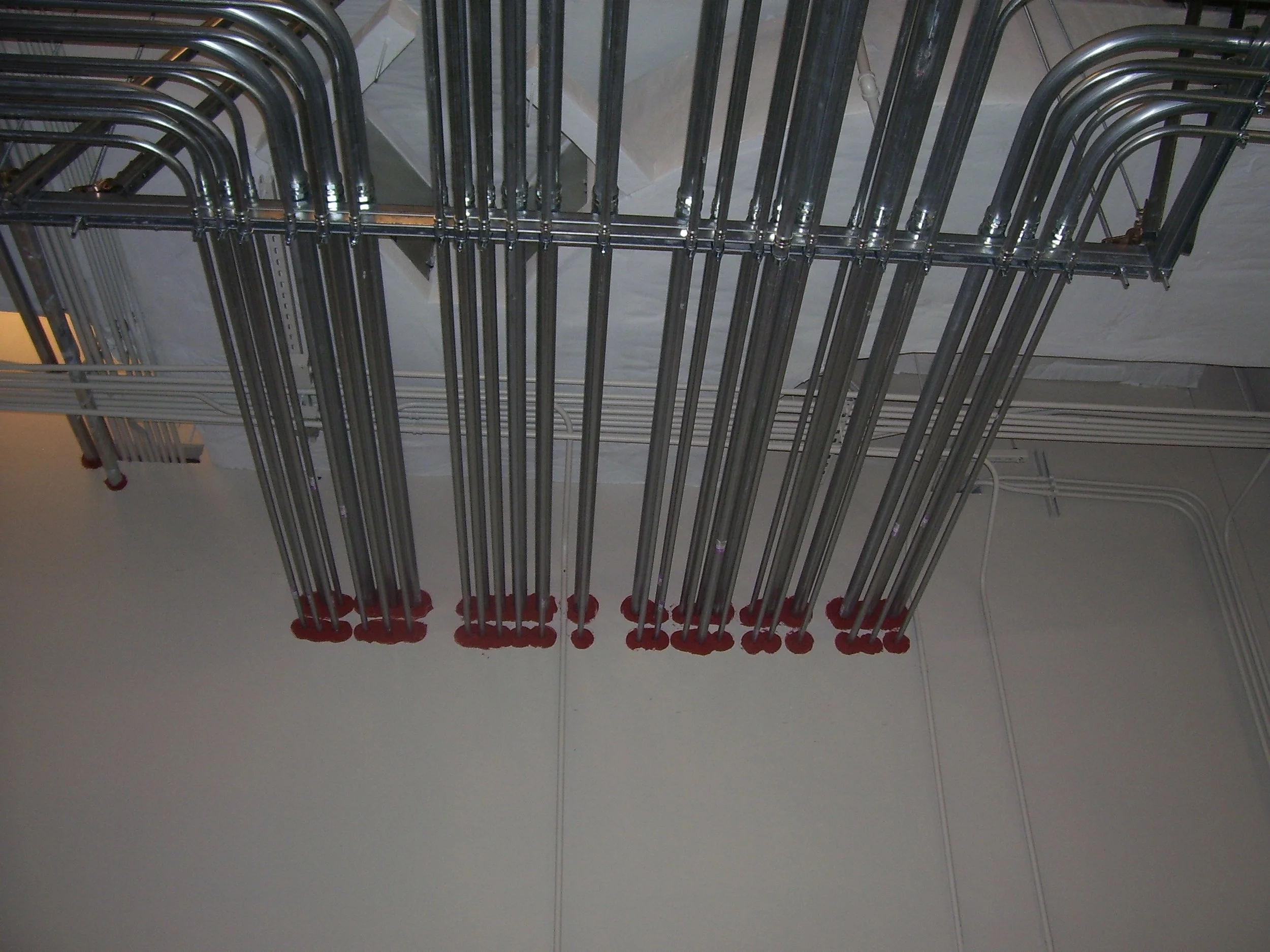 Metal conduit pipes through gyp wall with red fire stop caulking at penetrations