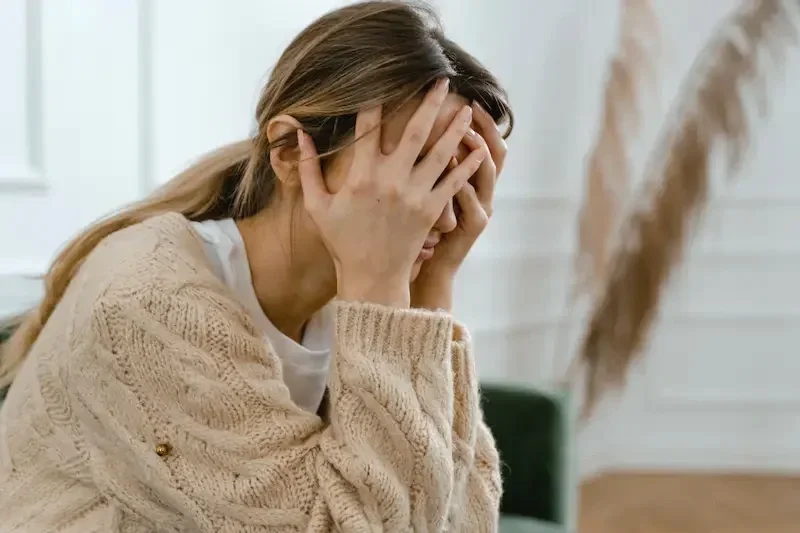 blonde-female-in-beige-sweater-holding-head-with-both-hands-covering-her-eyes-from-stress