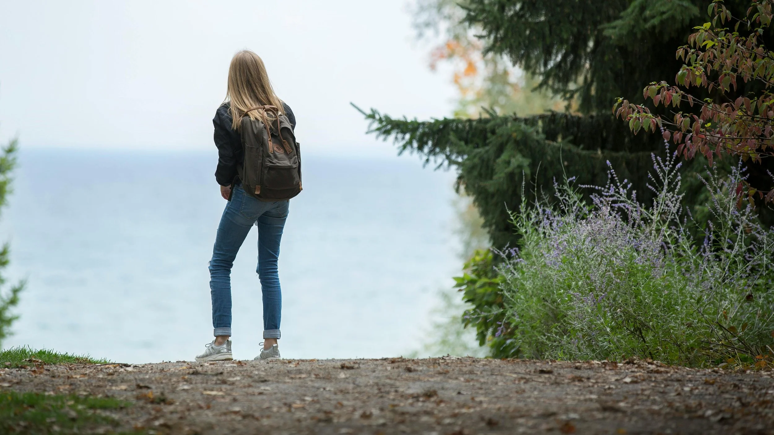 female-standing-looking-out-at-ocean-near-trees