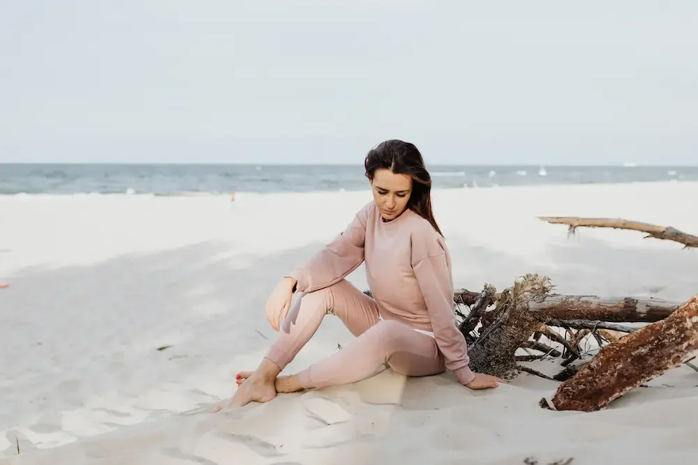 female-sitting-on-beach-driftwood-looking-down-away-from-ocean