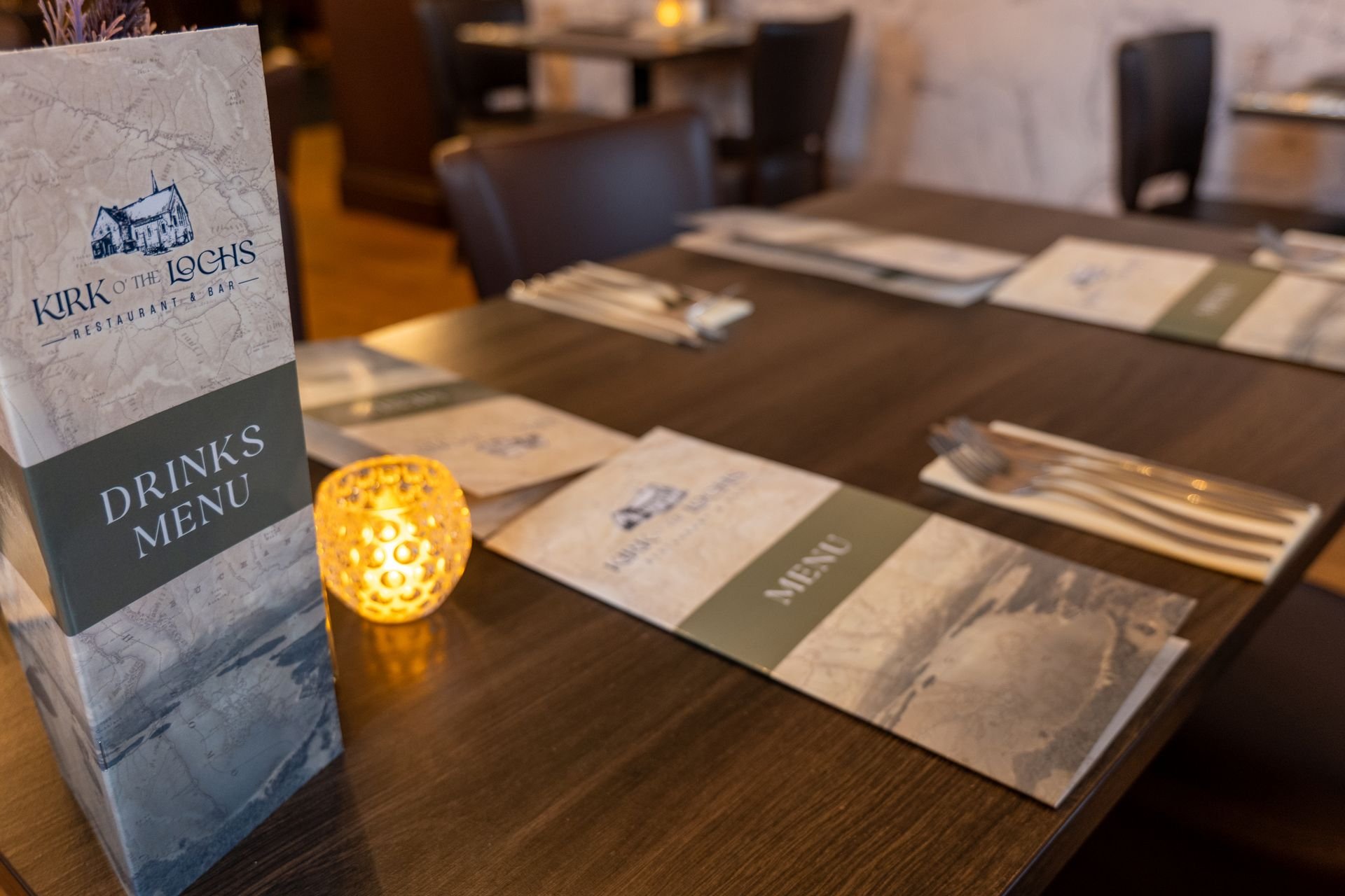 Restaurant table setting with menus, utensils, and a lit candle.