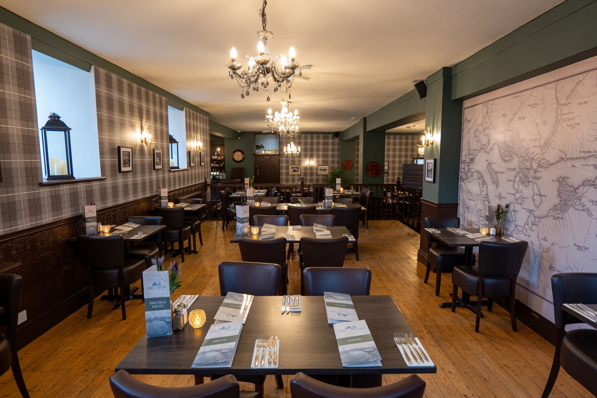 Kirk O' the Lochs restaurant interior with checkered wallpaper, chandeliers, neatly set tables, wooden flooring, and a wall map decoration.