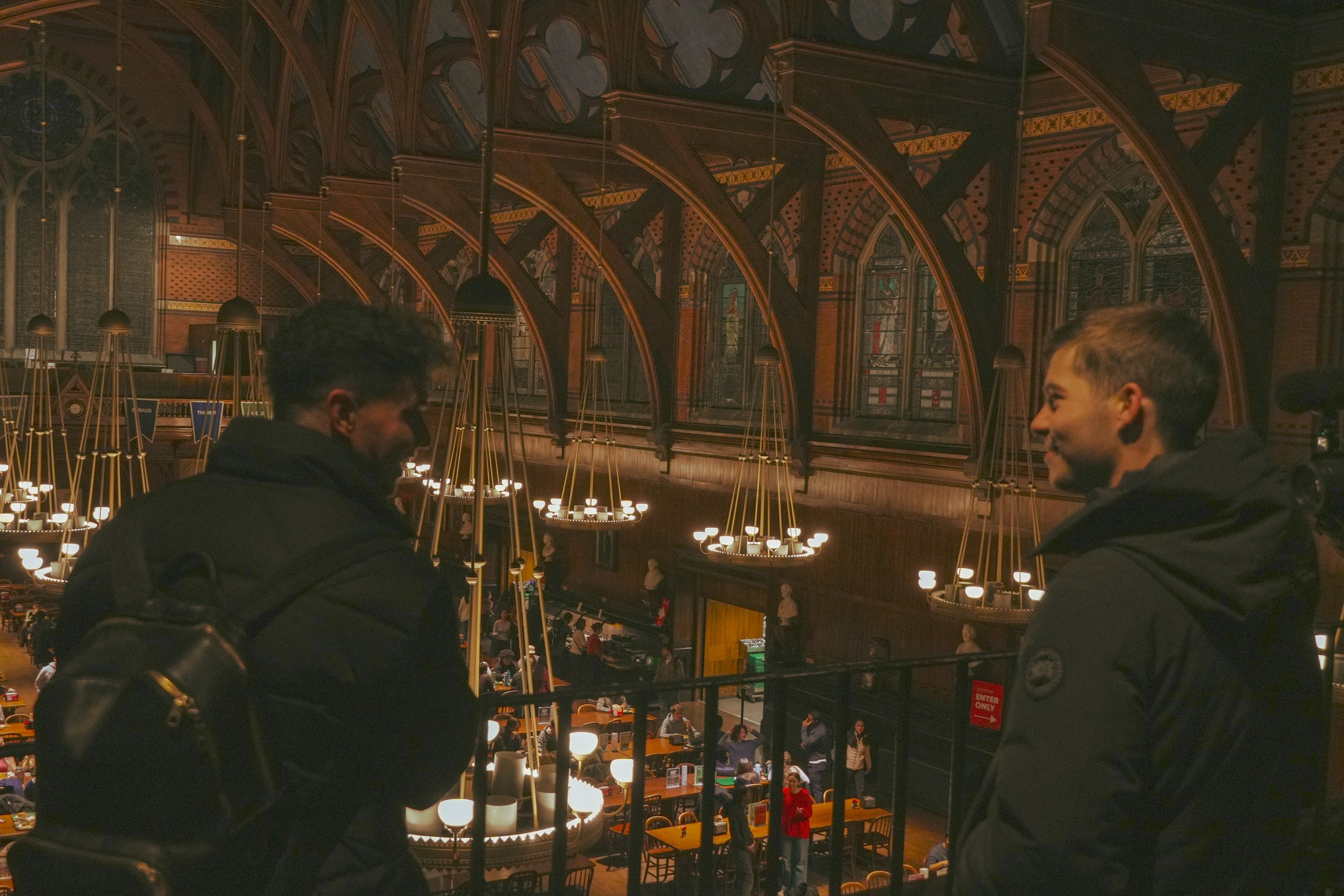 Two people in a dimly lit, ornate library with stained glass windows and chandeliers.