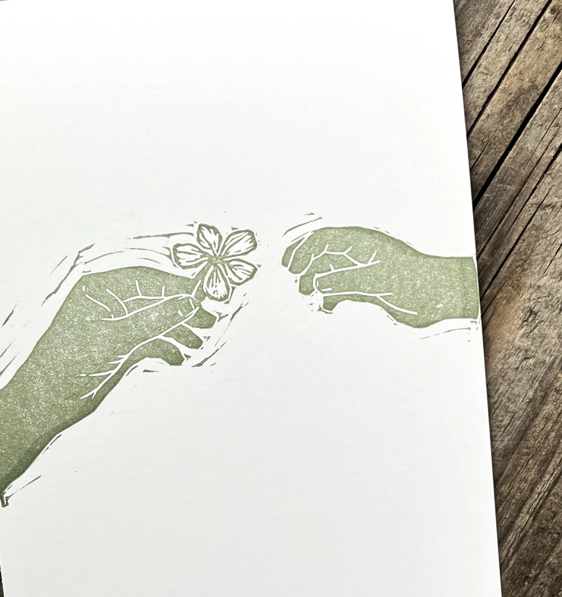 Illustration von zwei Händen, eine hält eine Blume, die andere bewegt sie. Die Zeichnung ist in grün gehalten und auf Papier, auf einem Holztisch.