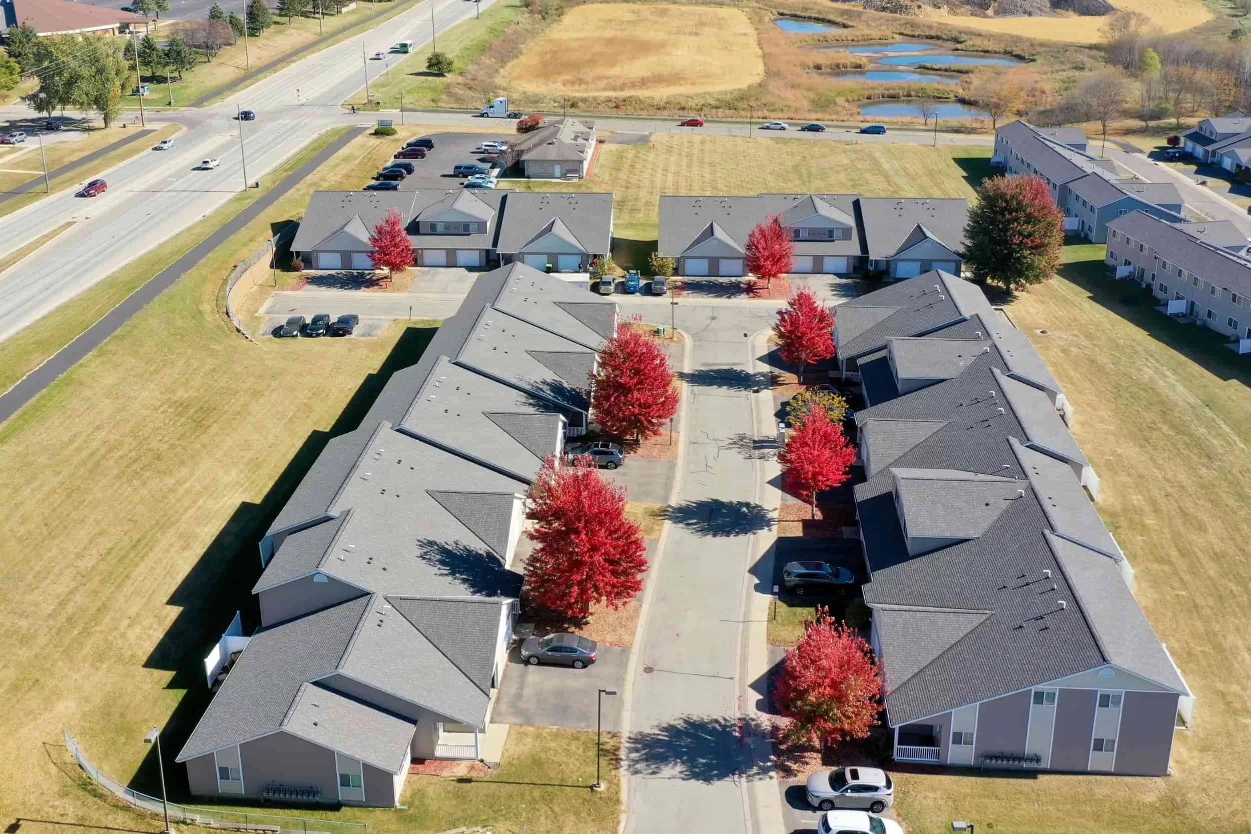 Aerial view of apartments in Rochester with red-leaved trees lining the driveway, set amid lush grassy fields.