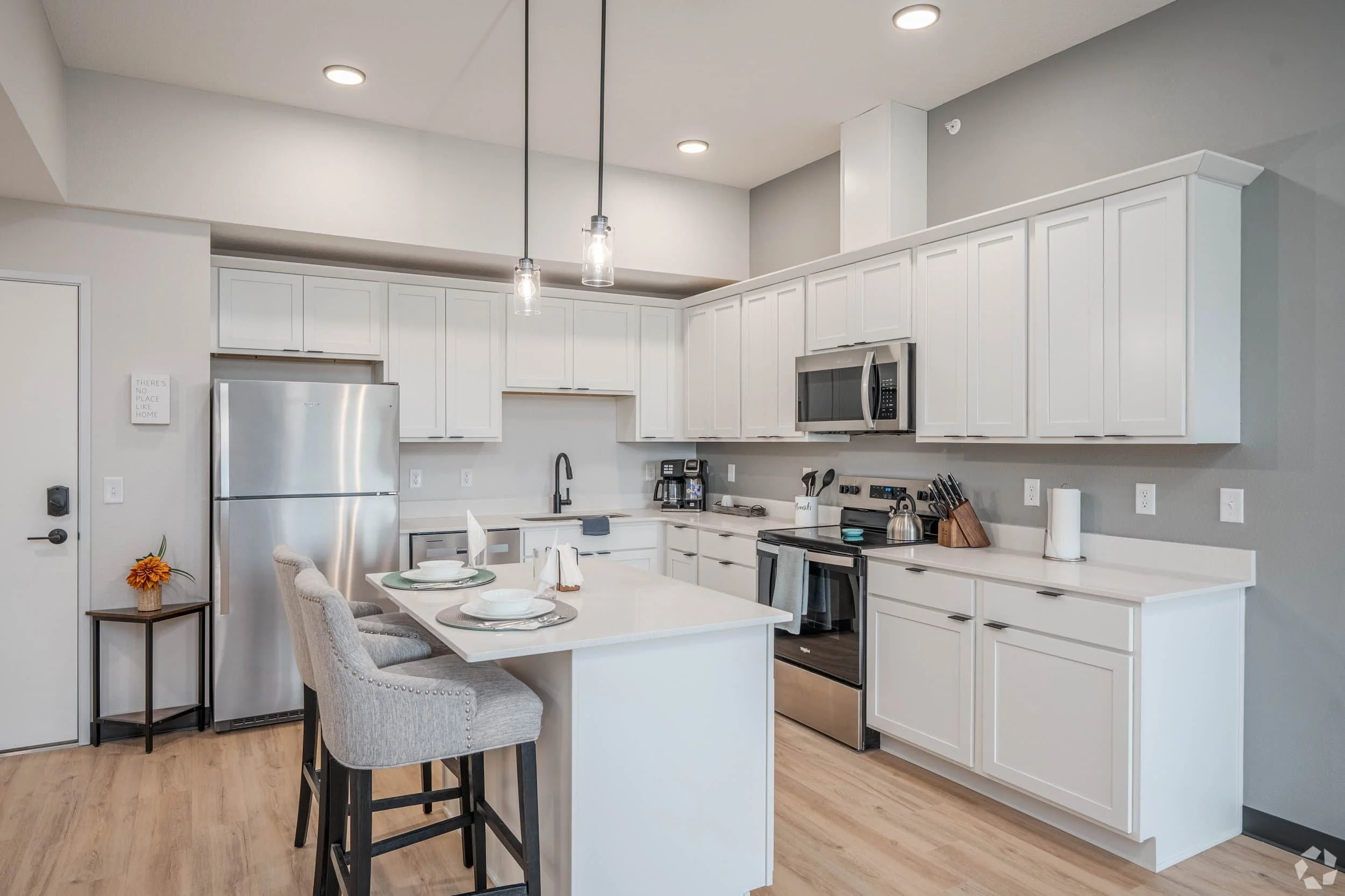 Modern white kitchen in apartments in Rochester, with stainless steel appliances, island seating, and pendant lights above.