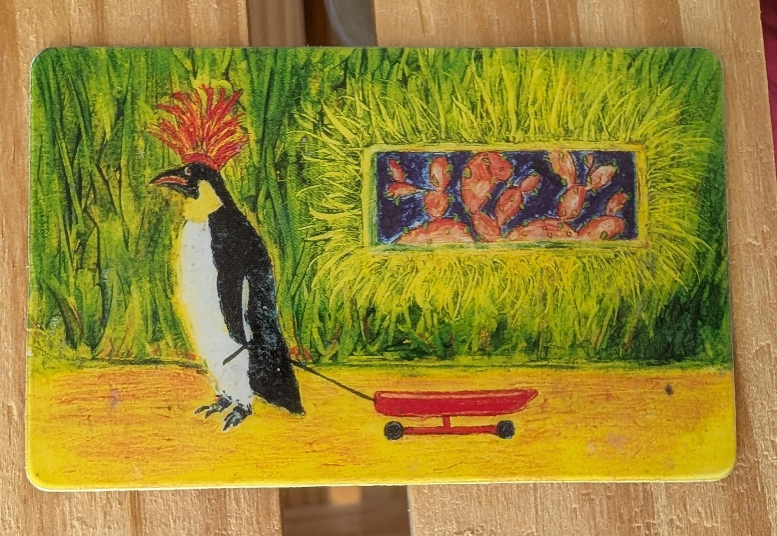 Brightly colored library card depicting a penguine in a red feather headress pulling a red wagon in front of a green grass wall with art on it