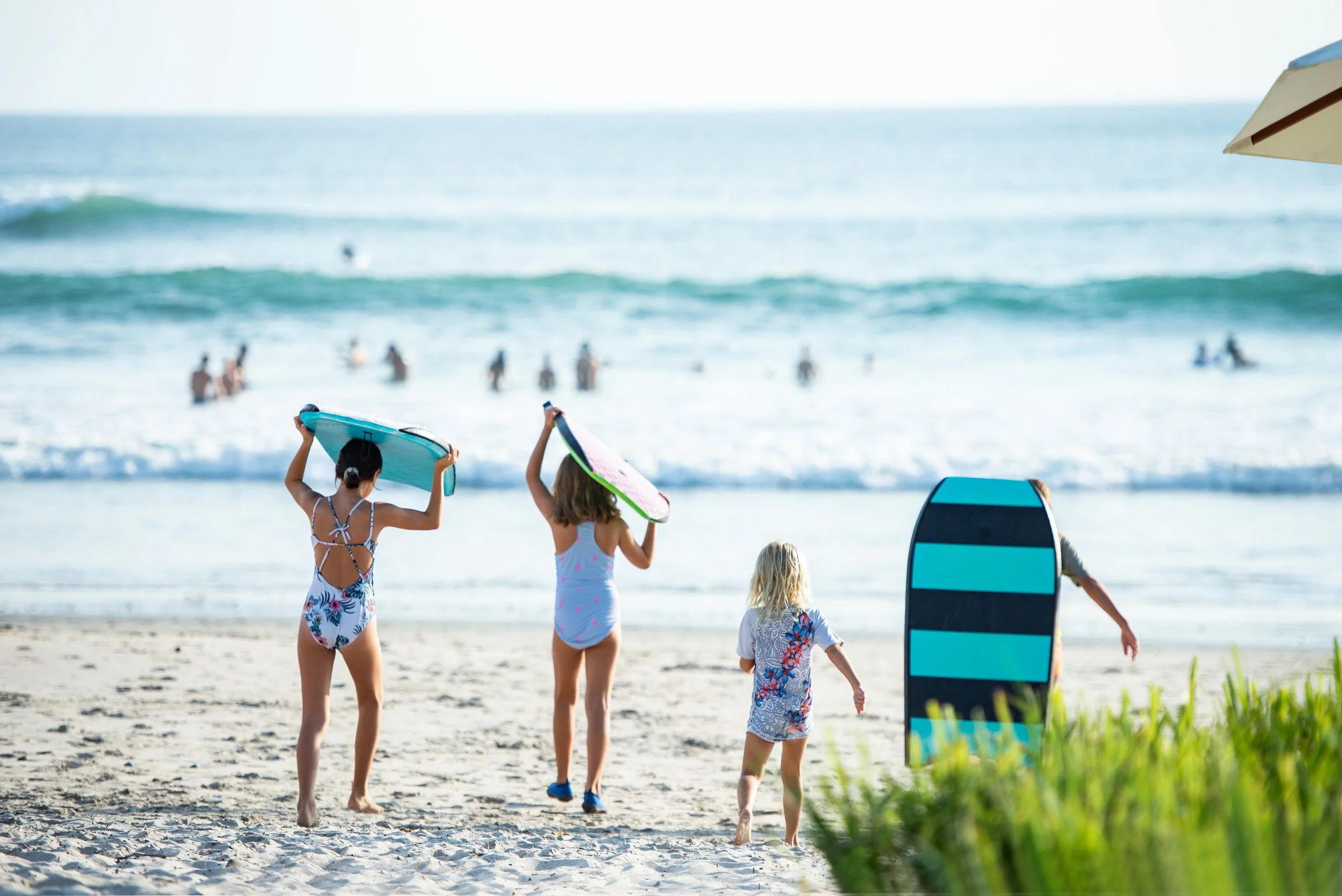 Children at the beach carrying boogie boards towards the ocean.