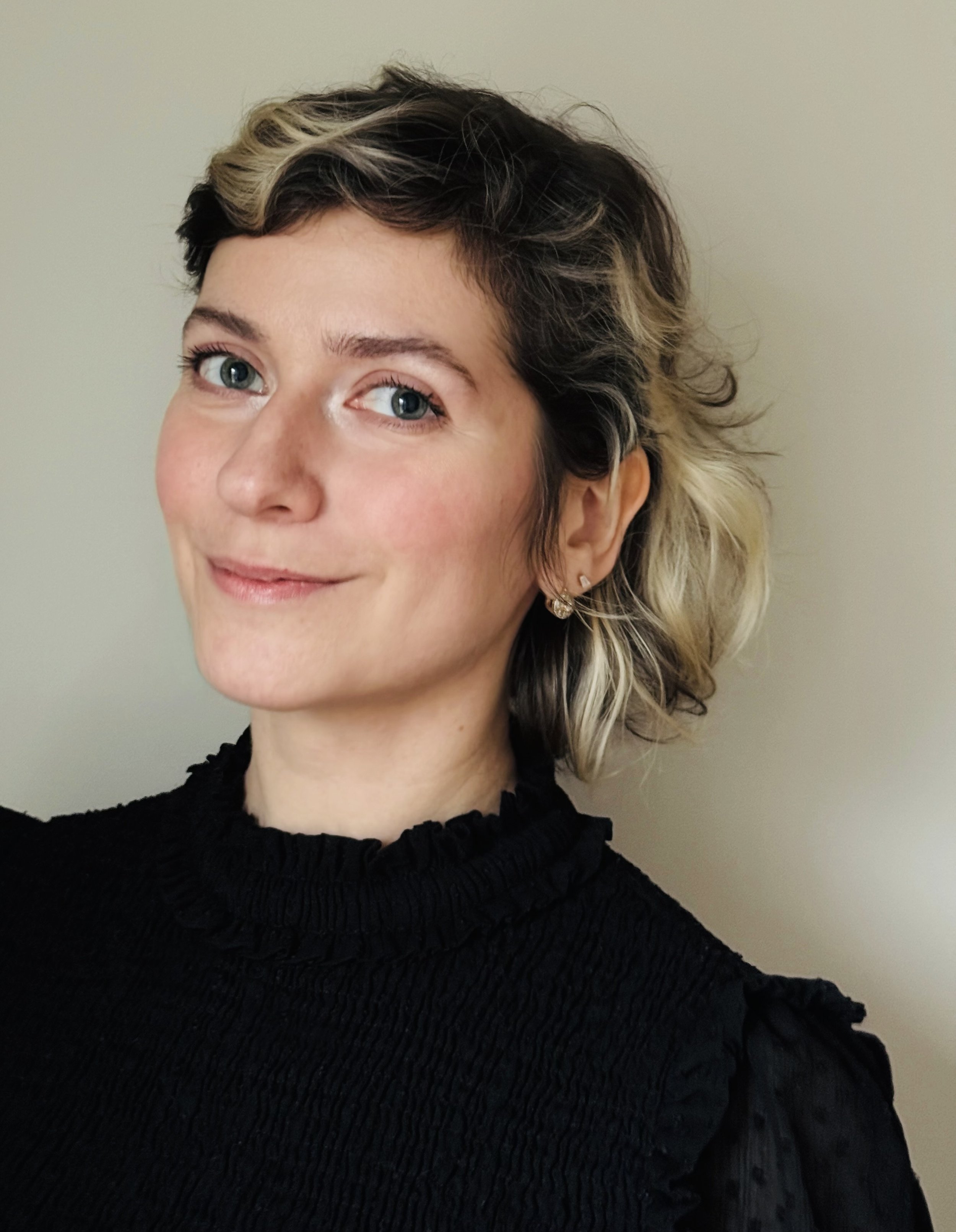 Katja Ryabtseva professional headshot portrait, smiling woman with shoulder length curly blonde and brown hair and a black blouse.