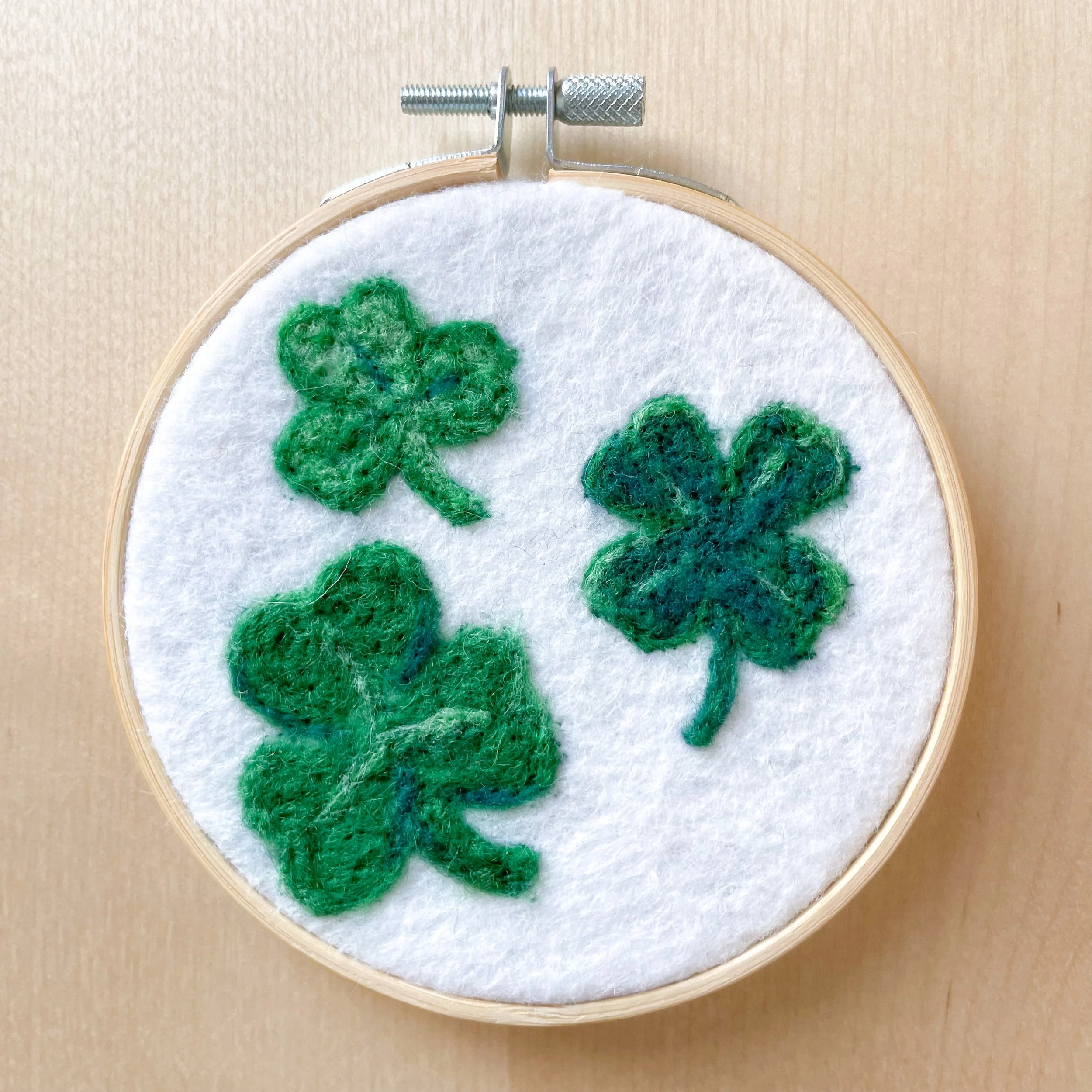 Felted art with three small shamrocks framed in an embroidery hoop.