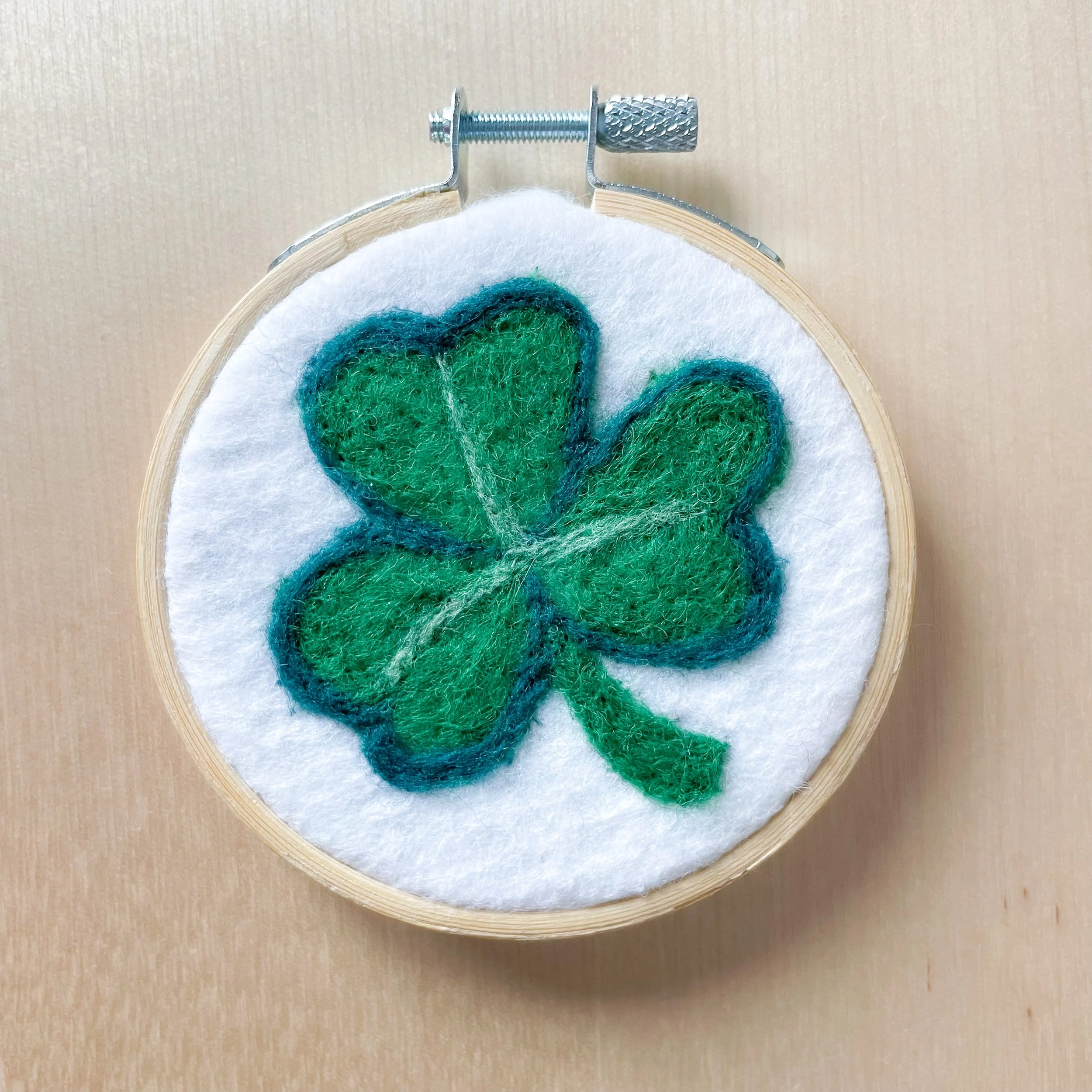 Felted shamrock art framed in an embroidery hoop.