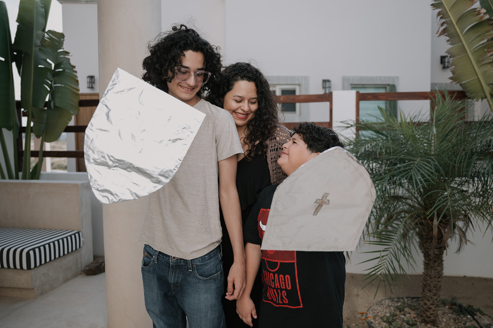 Mother and sons stand in a smiling embrace holding shields crafted with aluminum from a Conscious Care Cards connection activity.