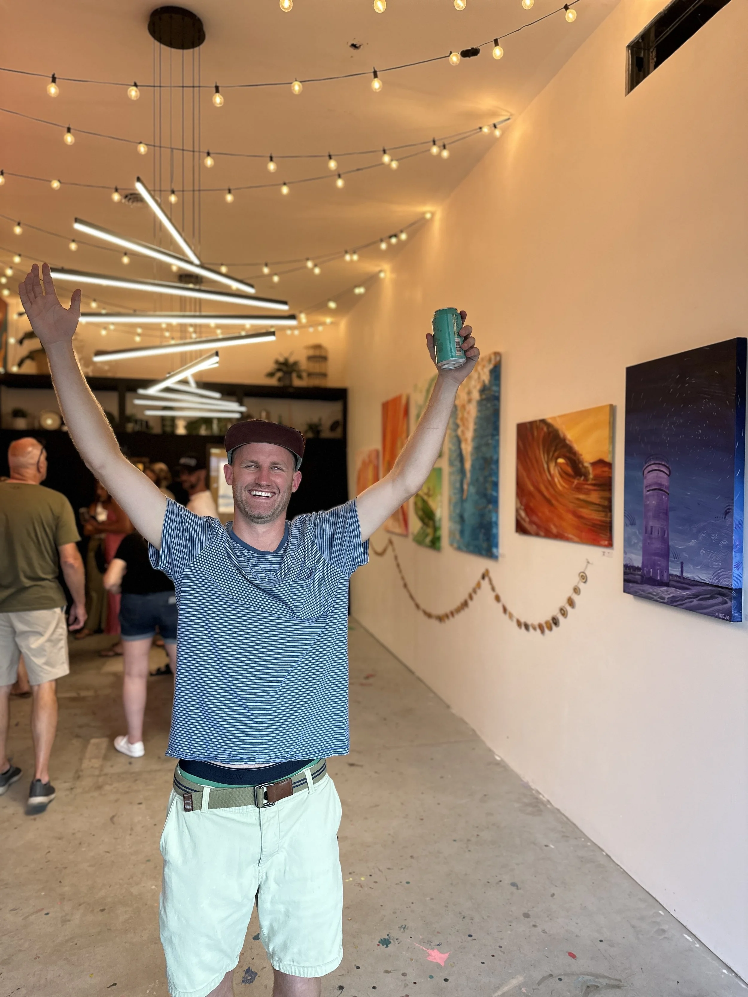 Interior of a library or bookstore with a large colorful mural depicting a countryside scene above empty shelves and a person standing with arms outstretched.