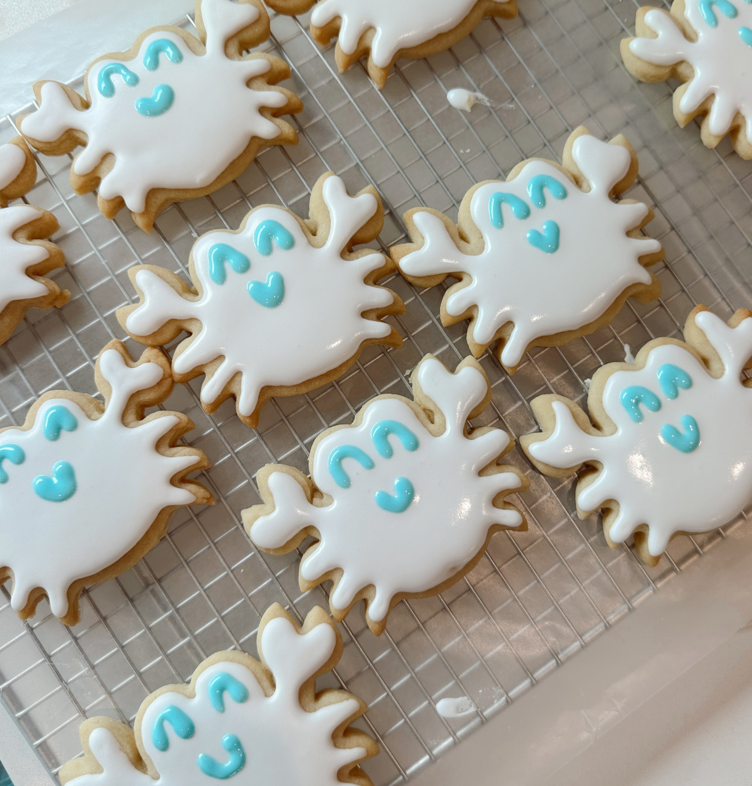 Cookies decorated as snowflakes with white icing and blue icing details on a cooling rack.
