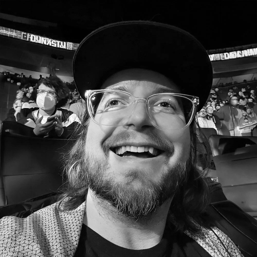 A black and white portrait photo of Sit Down Shut Up Mark Out host Blade Daily smiling at a live event.