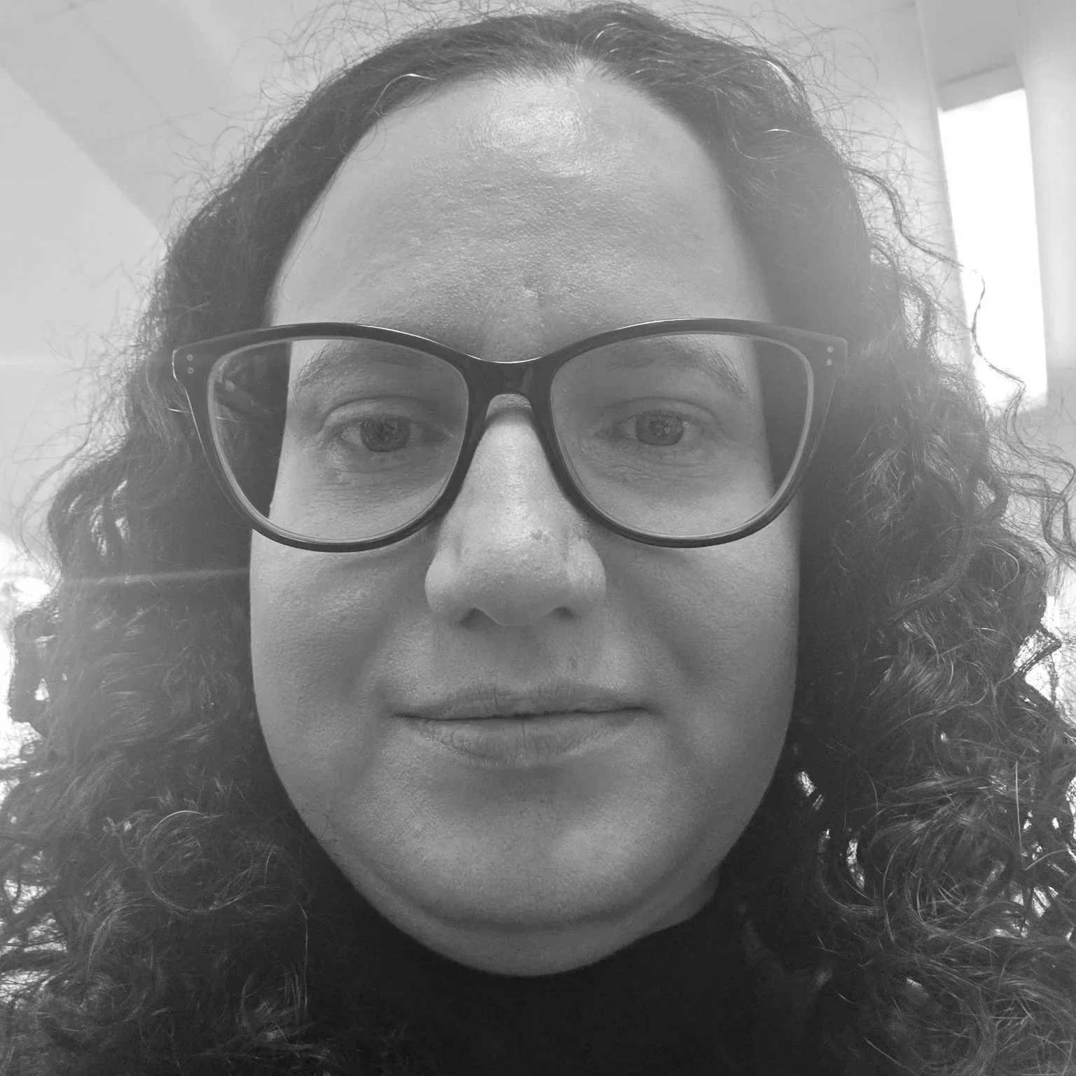 A black and white close-up photo of a woman with curly hair wearing glasses.