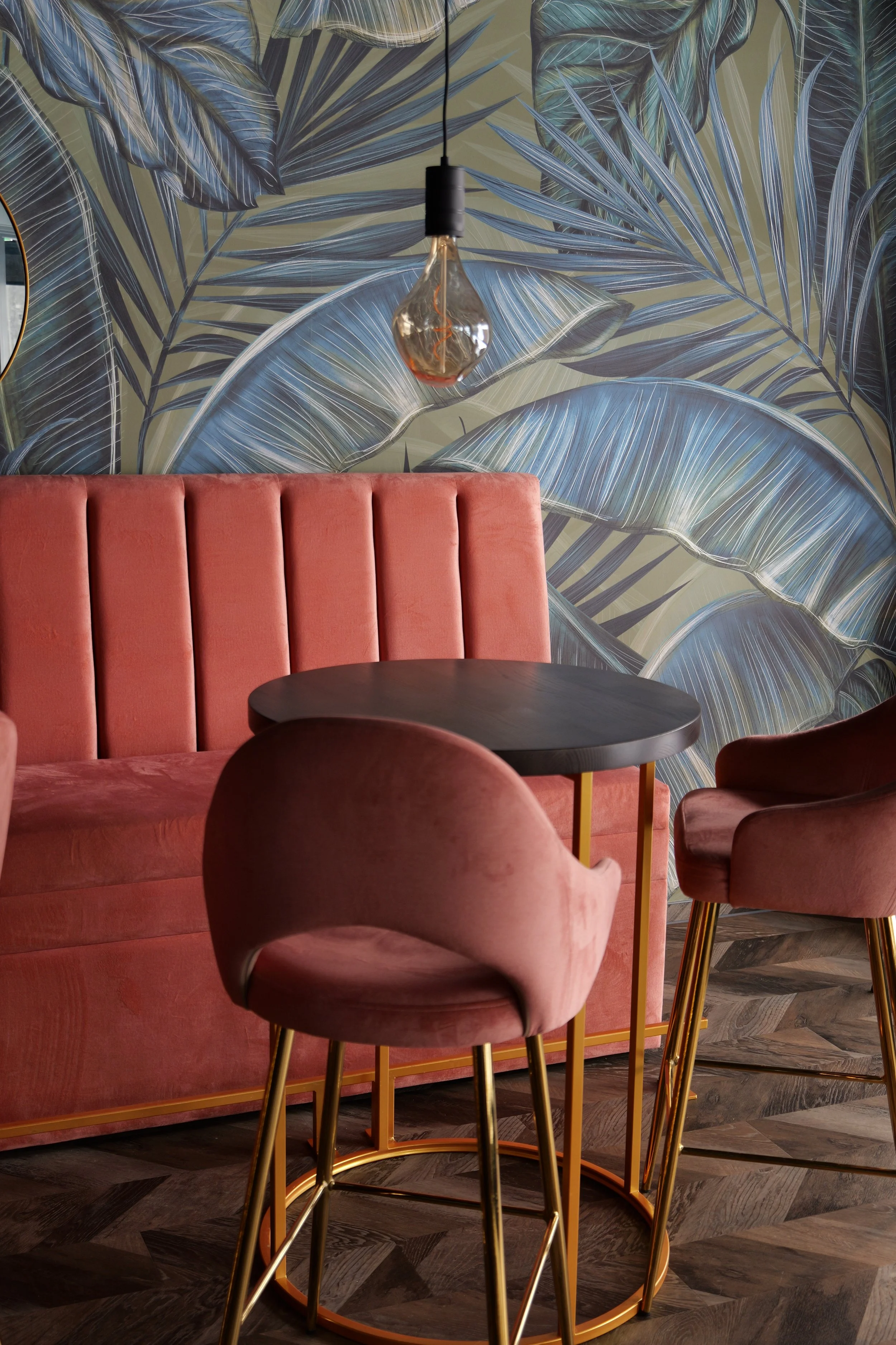 Stylish lounge area with pink upholstered chairs, round wooden tables, and a pink velvet banquette, decorated with wall mirrors and pendant lights.