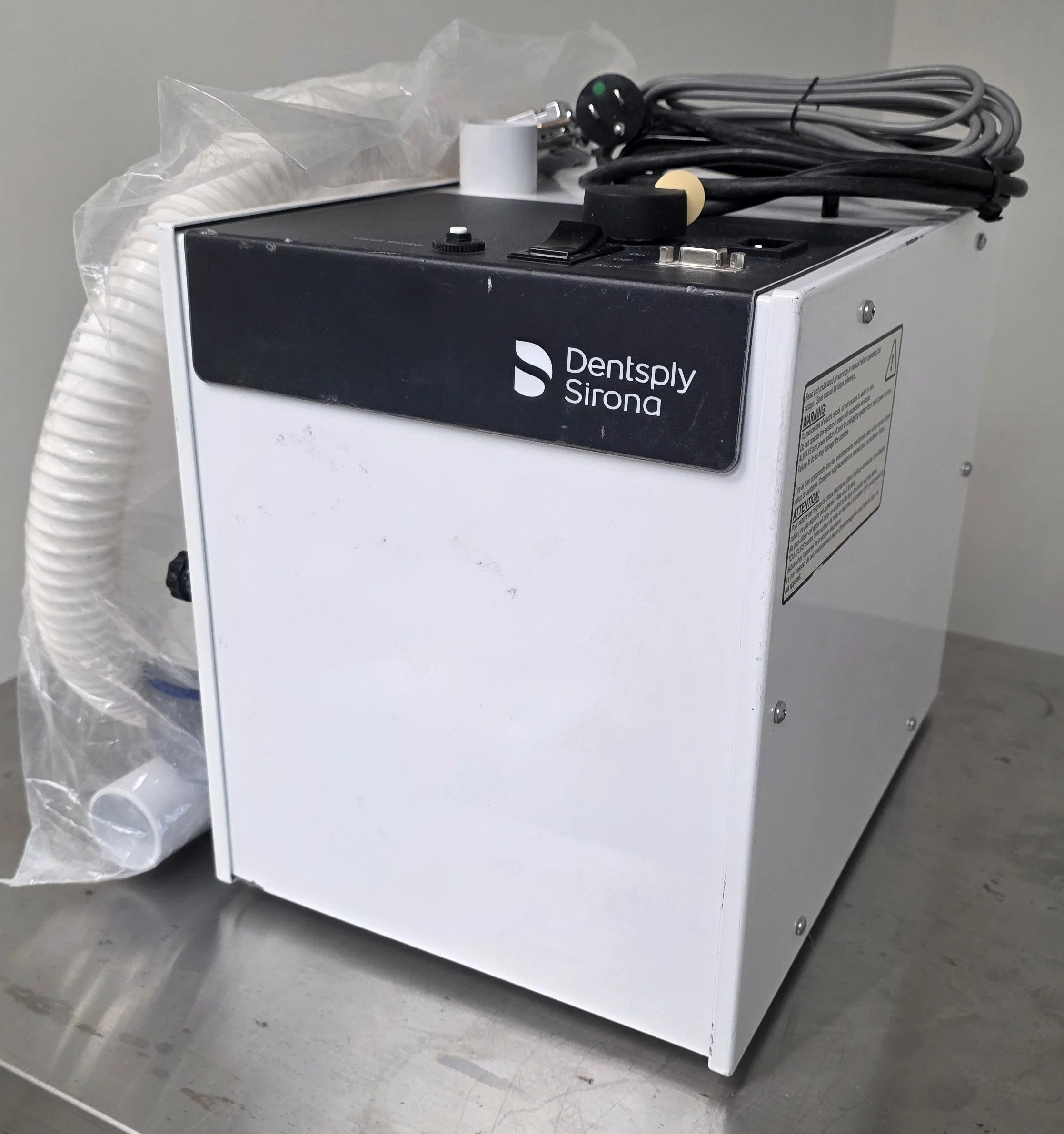 A Dentsply Sirona dental device on a metal surface with connected power cords and a tube.