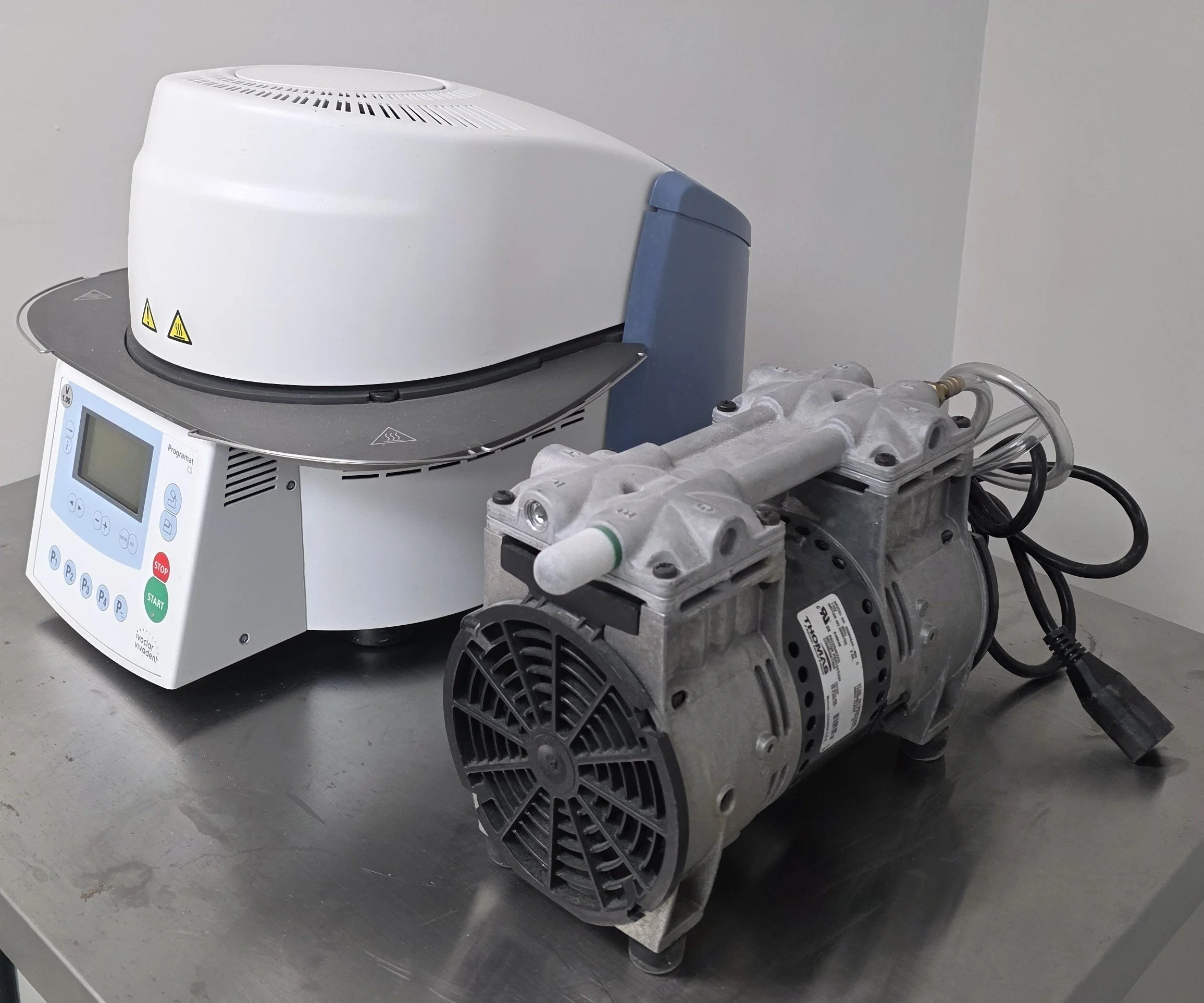 Laboratory equipment with a white and gray machine connected to an electric motor on a stainless steel table.