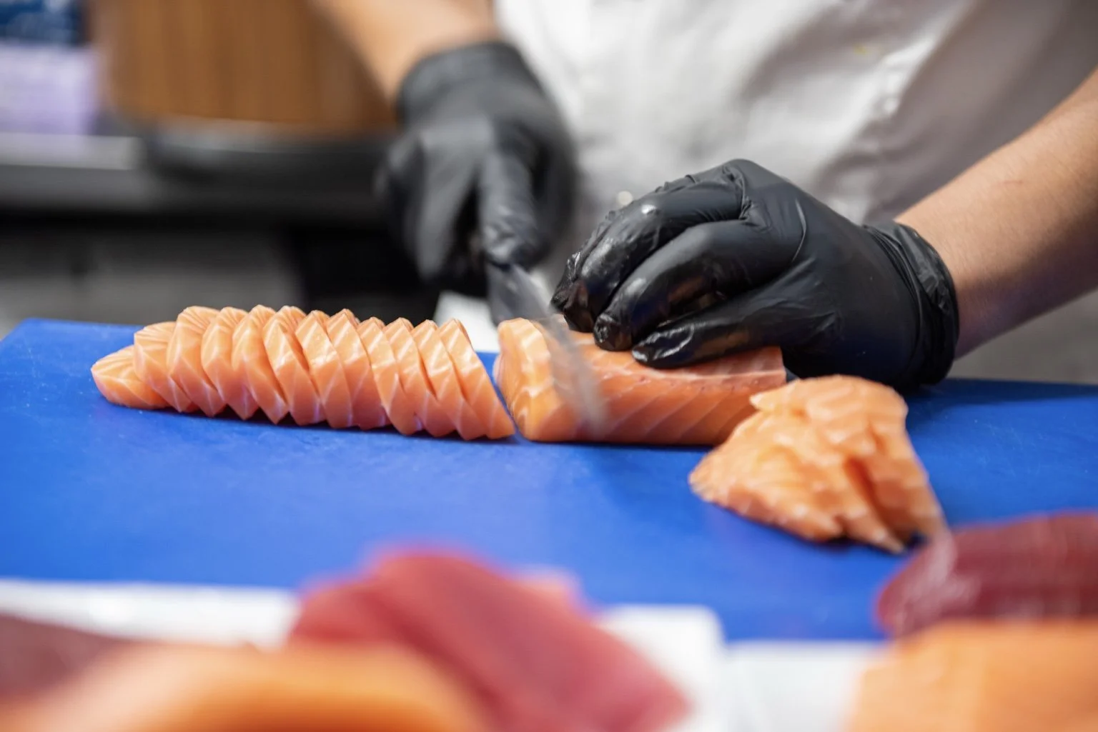 Sushi chef slicing fresh salmon sashimi in the Sushi & Salad kitchen.