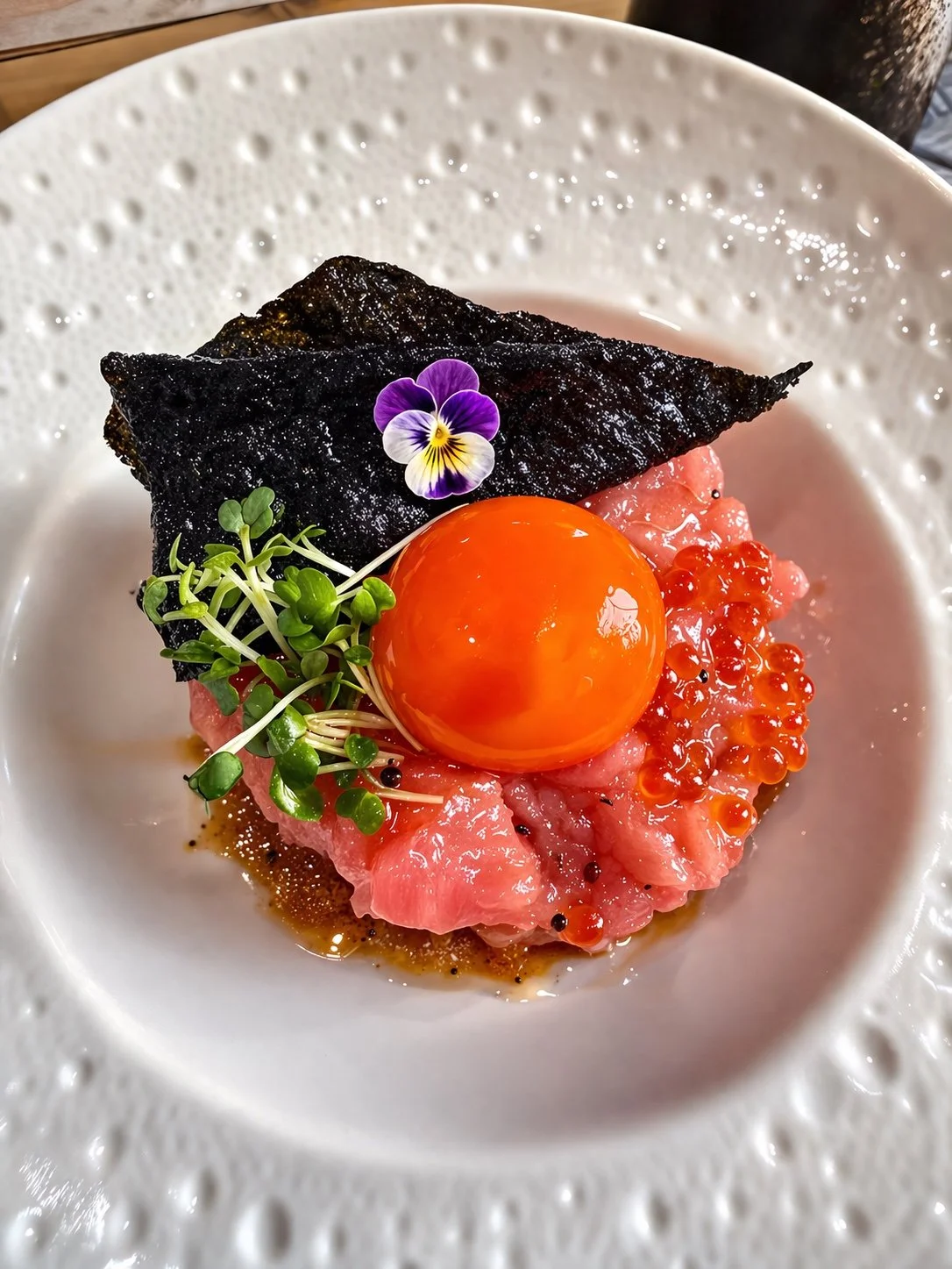 Finely diced fish topped with an egg yolk, nori, microgreens and an edible flower.