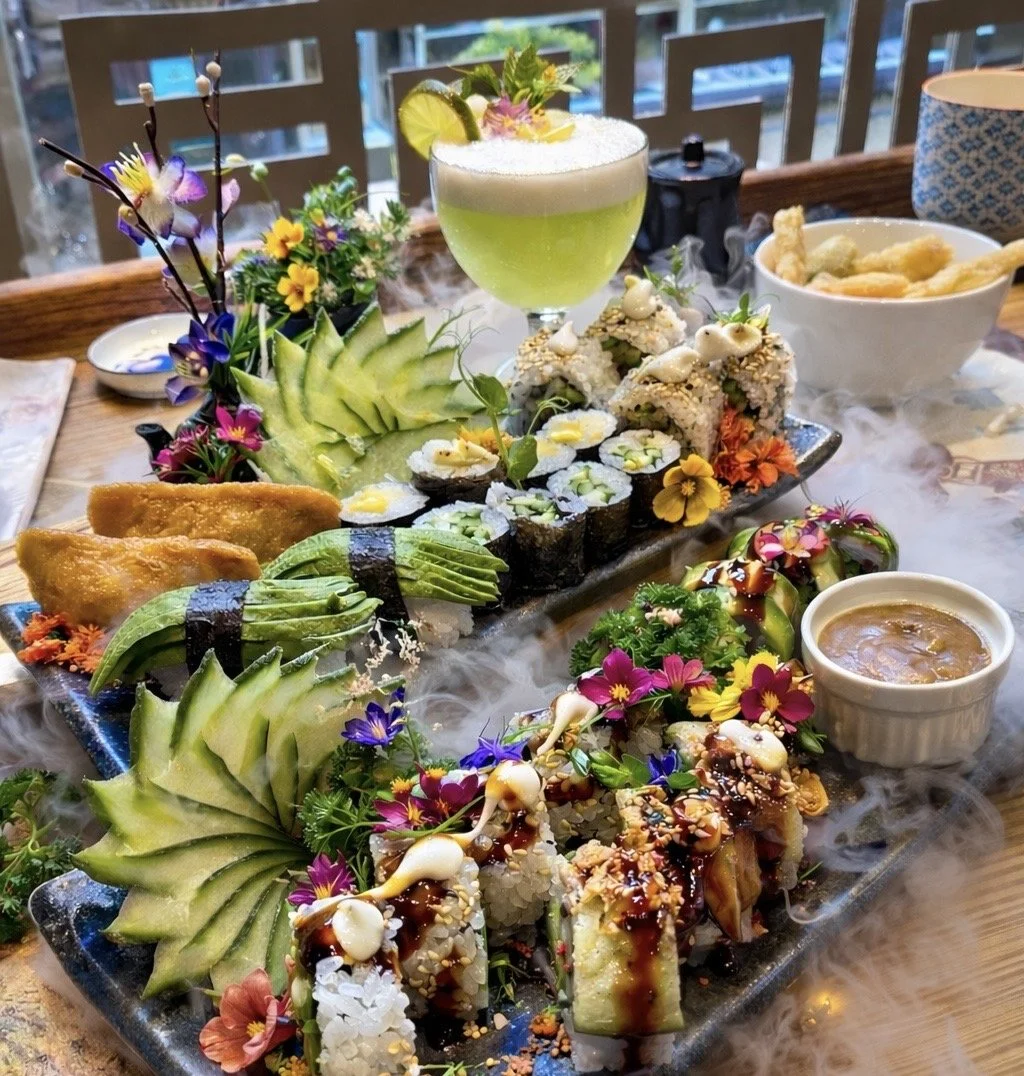 Sushi and vegetable rolls with carved cucumber garnishes, edible flowers and a green cocktail.