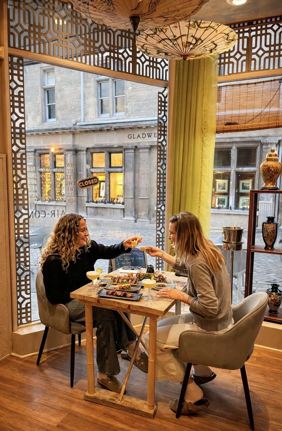 Two guests enjoying a meal beside the tall restaurant windows at Sushi & Salad.