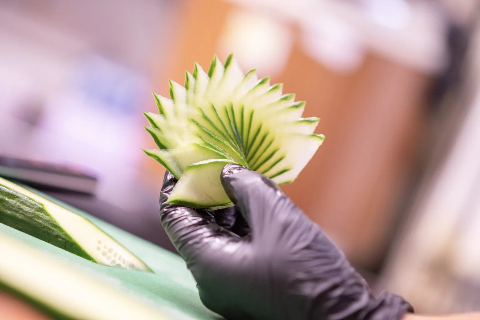 Sushi chef creating a decorative cucumber garnish by hand.