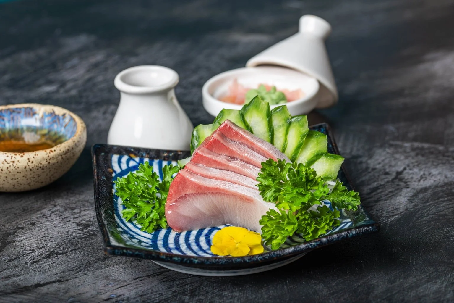 Fresh sashimi slices arranged with cucumber and green garnishes on a blue ceramic plate.