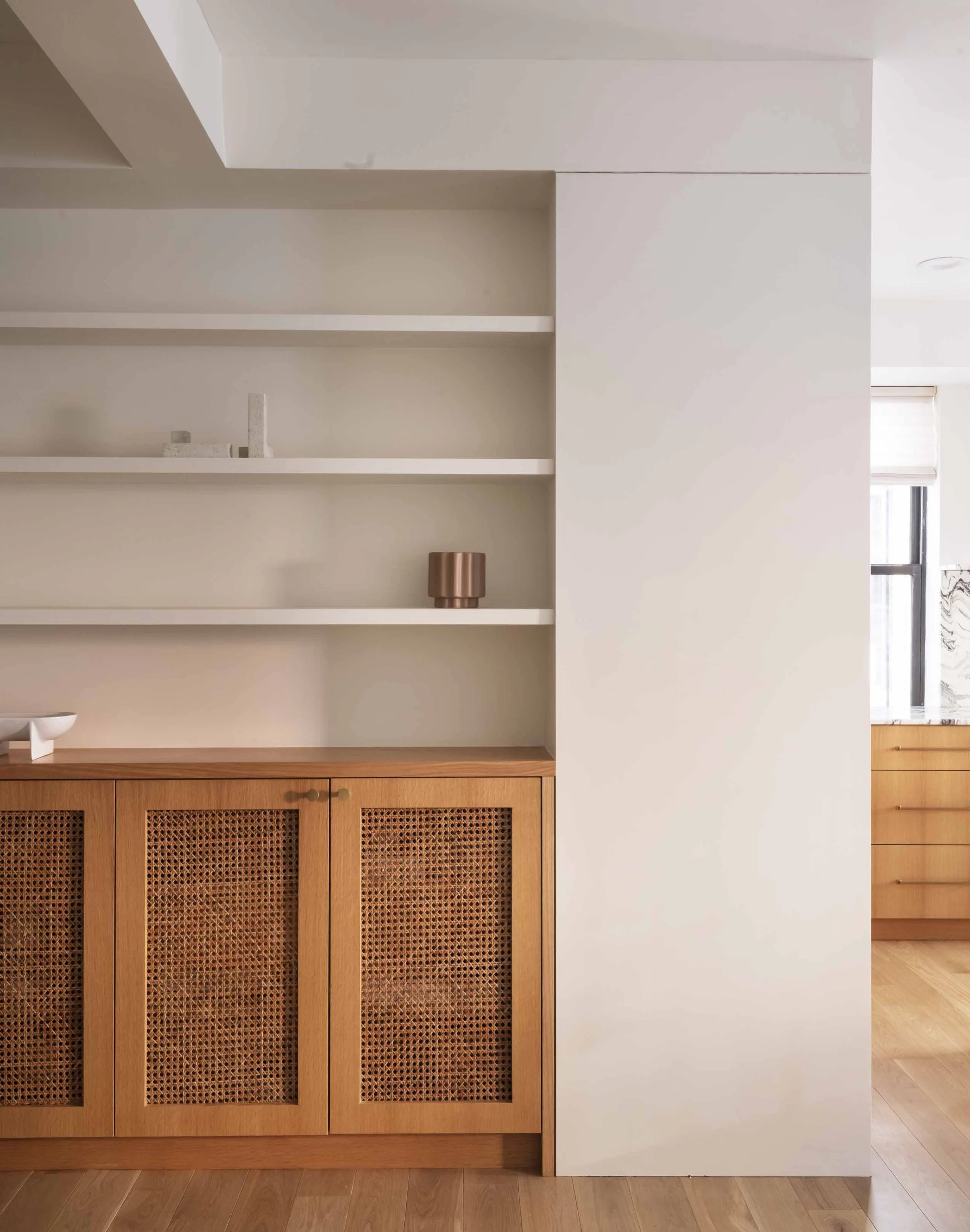 Interior of a room with wooden cabinets, white shelves, and a partial view of a window.