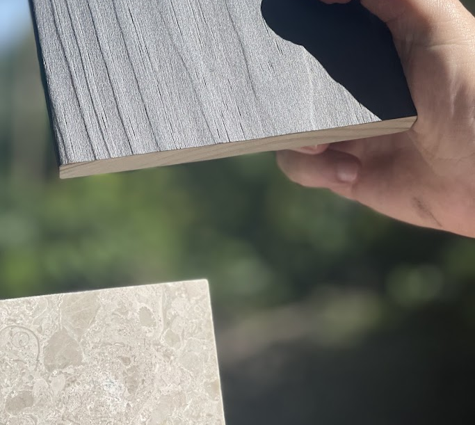Close-up of a person's hand holding a gray wooden plank over a stone surface outdoors.